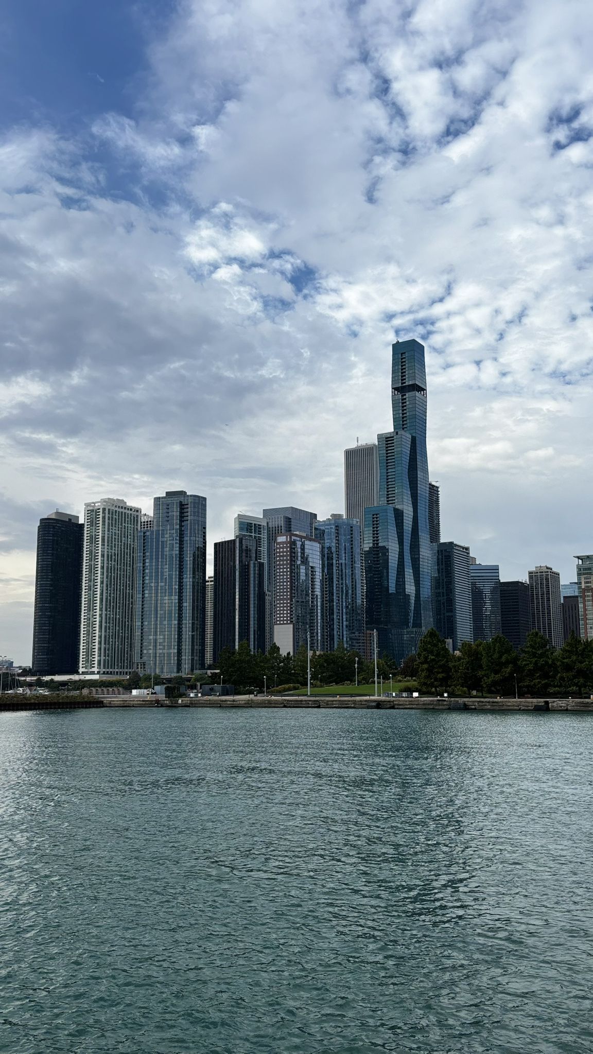 A dense city skyline rises from across the water under a cloudy sky. - Magnificent Mile and Navy Pier Walk