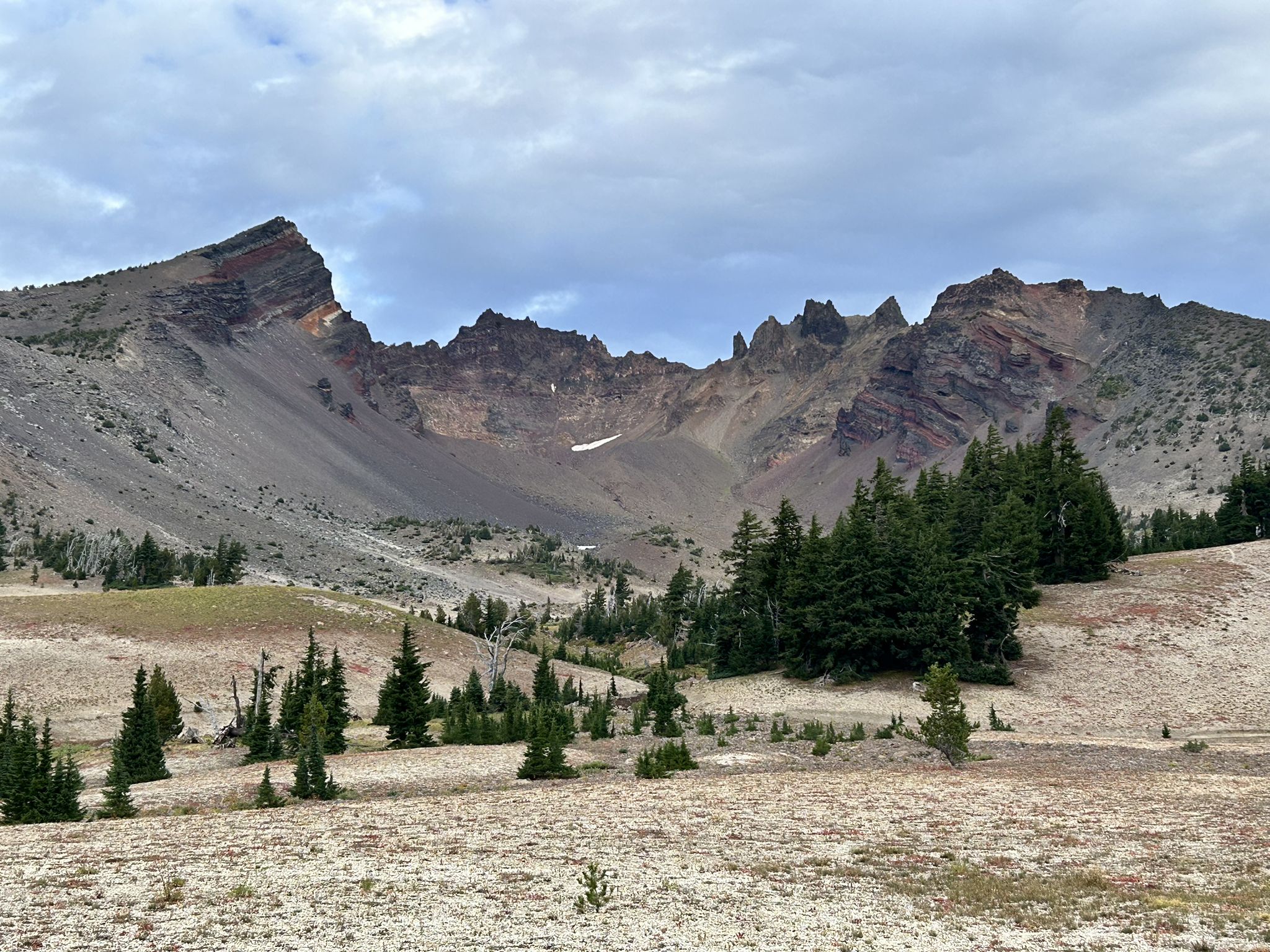 Valley with scattered trees, rocky mountains, and cloudy sky. - Broken Top Loop