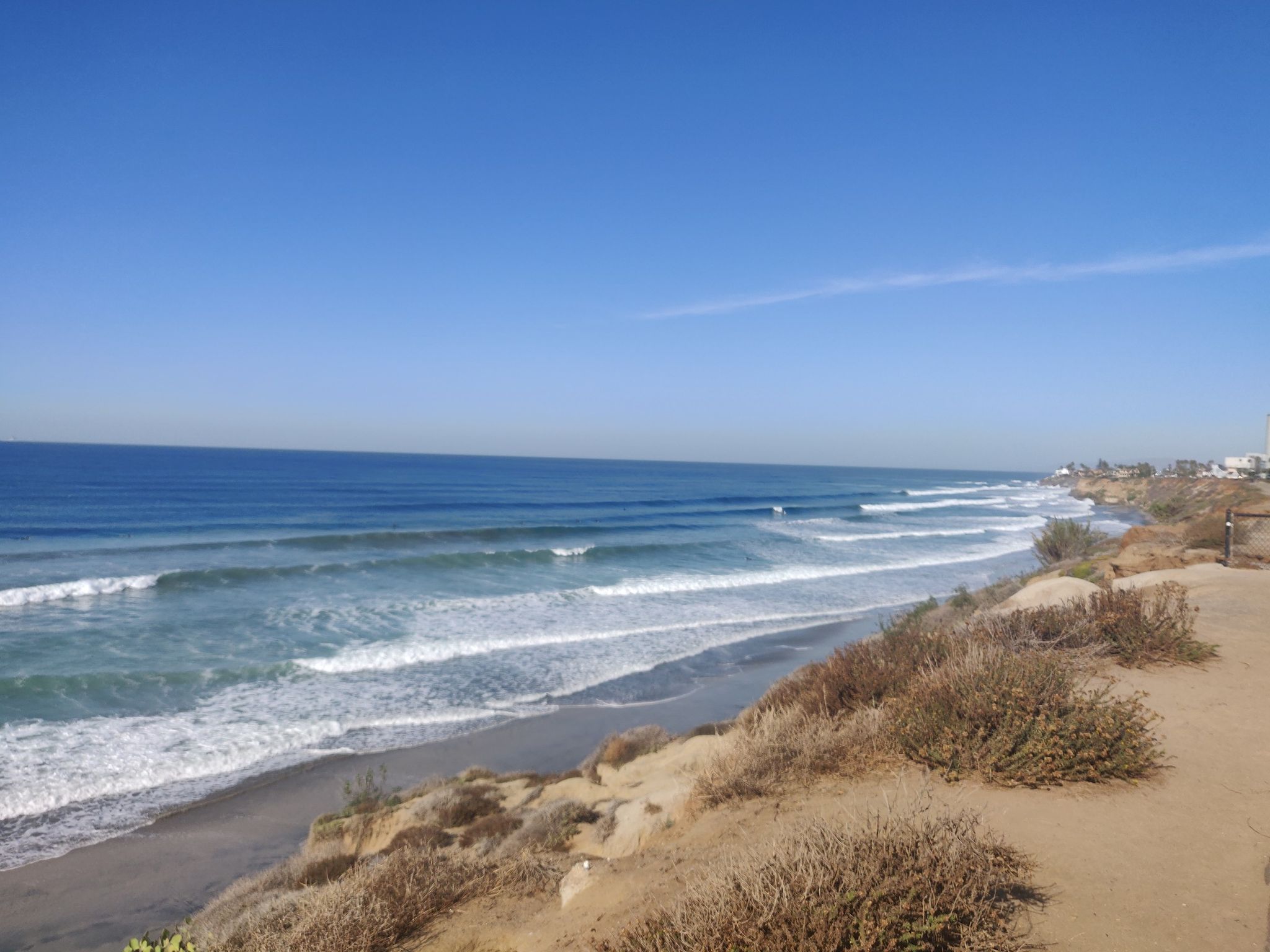 Bright day at a beach with gentle waves and a sandy cliff. - South Carlsbad Beach – South Carlsbad State Beach loop from McClellan-Palomar Airport