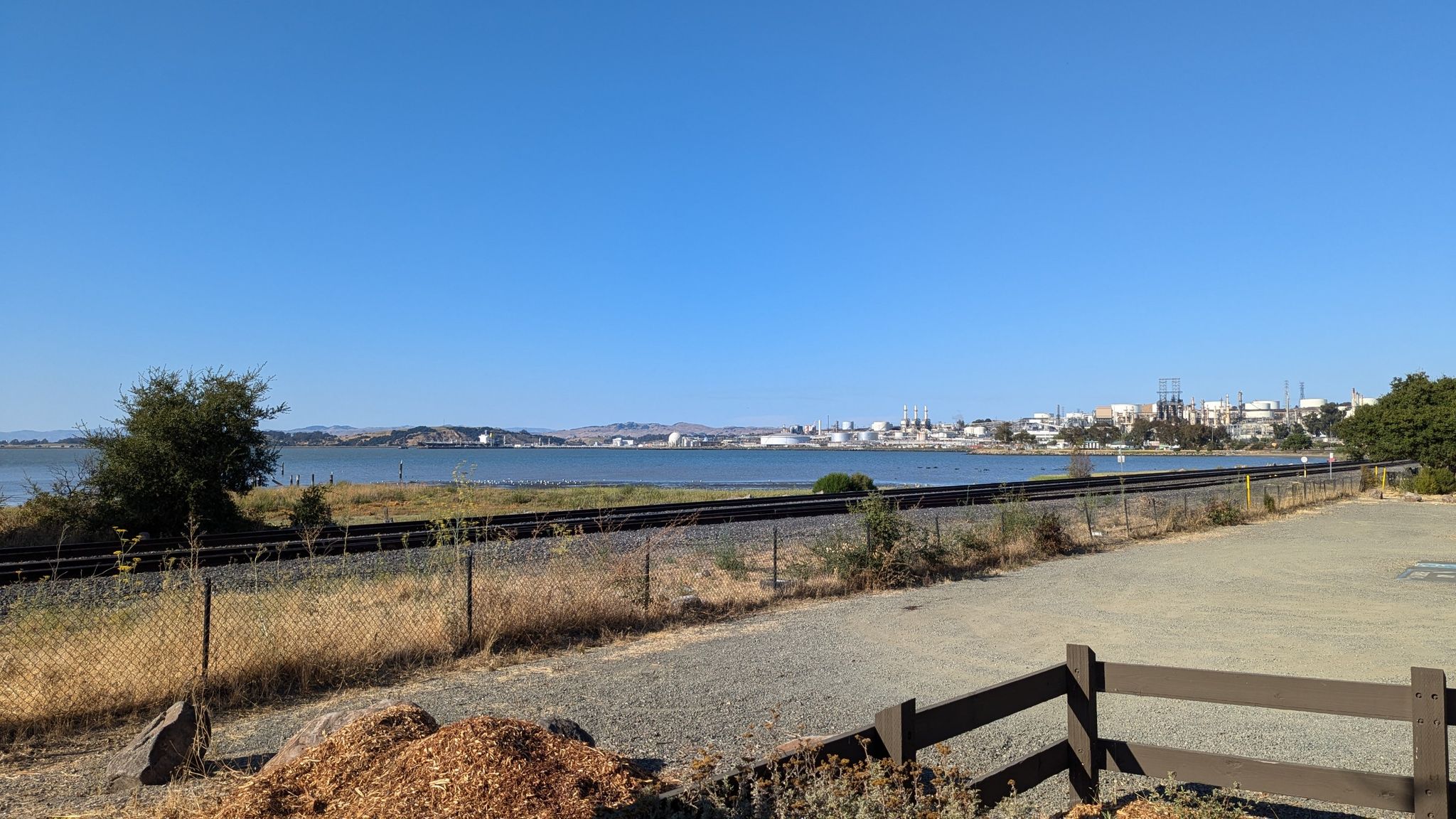 Clear day overlooking a body of water, railroad tracks, and a distant city. - Lone Tree Point Regional Park loop from Hercules
