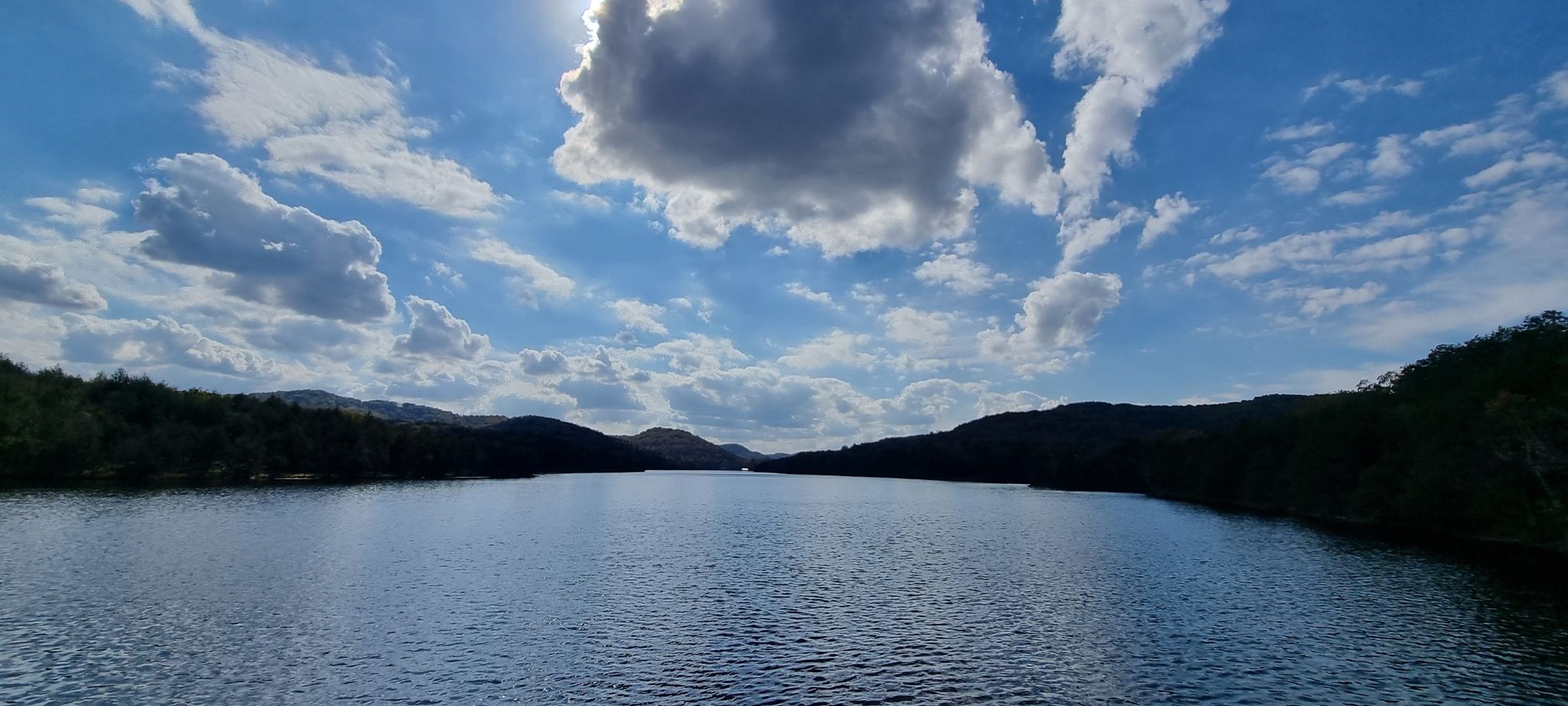 Wide shot of a calm lake surrounded by forested hills under a cloudy sky. - Lake Leatherwood Park – Lake Leatherwood Dam loop from Camp Office