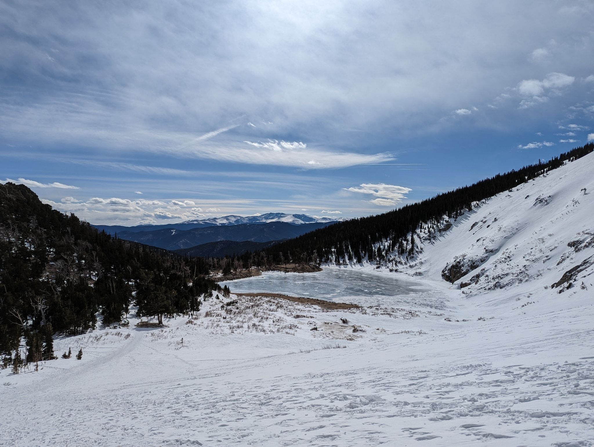 Snowy mountain landscape with a frozen lake under a cloudy blue sky. - St. Mary's Glacier Trail