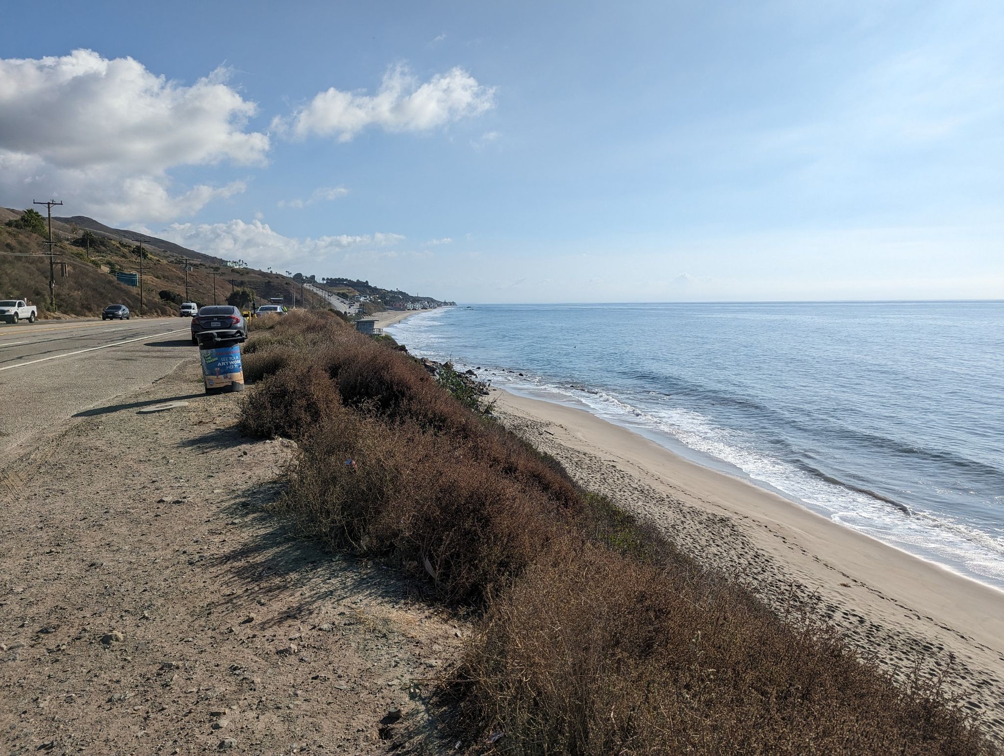 Coastal road alongside a sunny beach with ocean waves and distant cars. - Latigo Canyon Loop