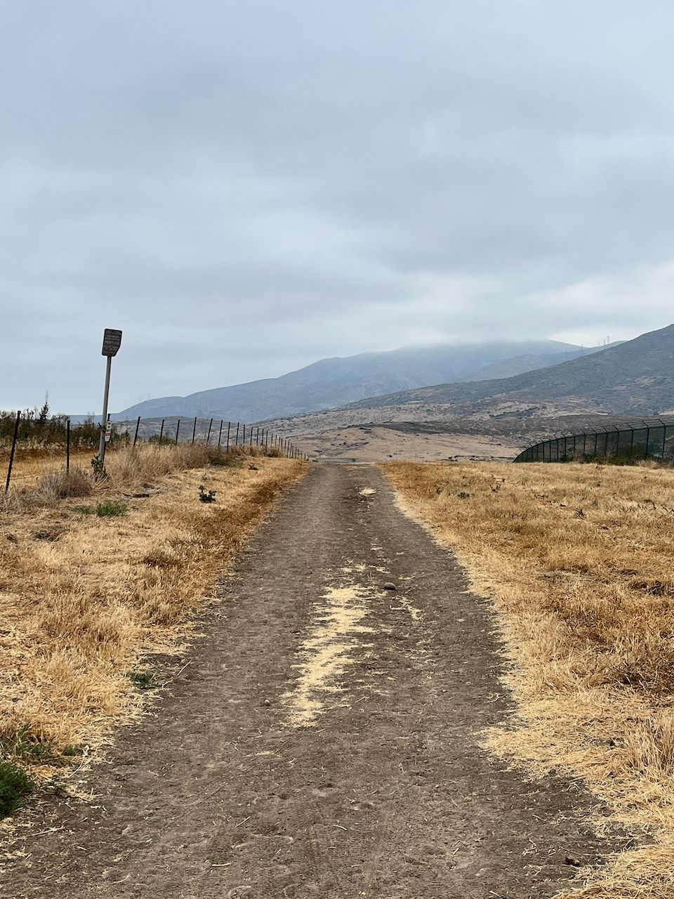A dirt path through dry grass leads towards distant, hazy mountains. - Mother Miguel Mountain from Sweetwater Reservoir