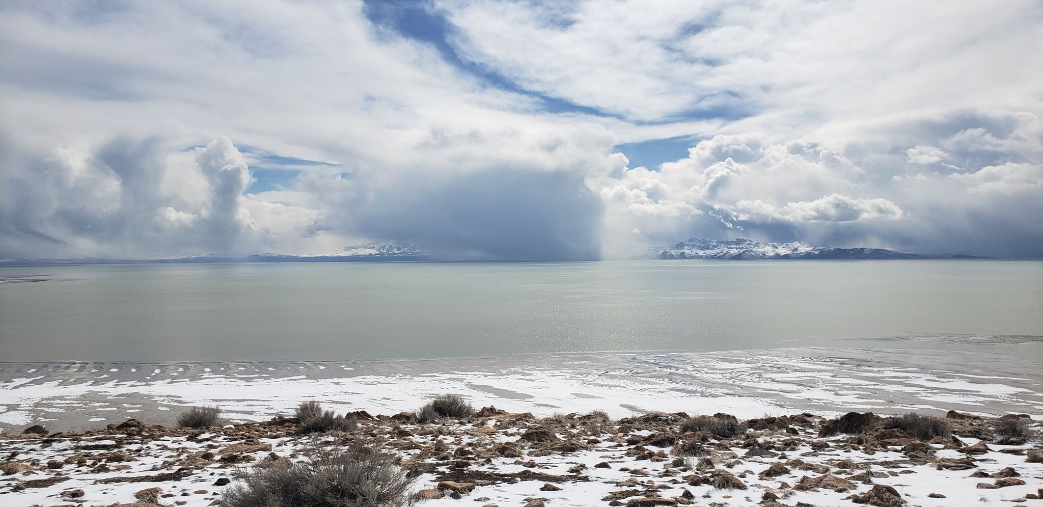 Calm lake with snowy shore under dramatic, cloudy skies and distant mountains. - Buffalo Point Trailhead – Buffalo Point loop from Buffalo Point