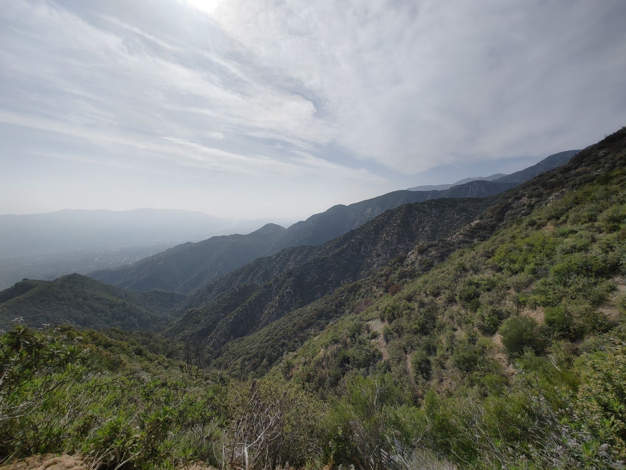Expansive view of green, hazy mountain ranges under a partly cloudy sky. - Angeles Overlook – Angeles Crest vista point loop from La Cañada Flintridge