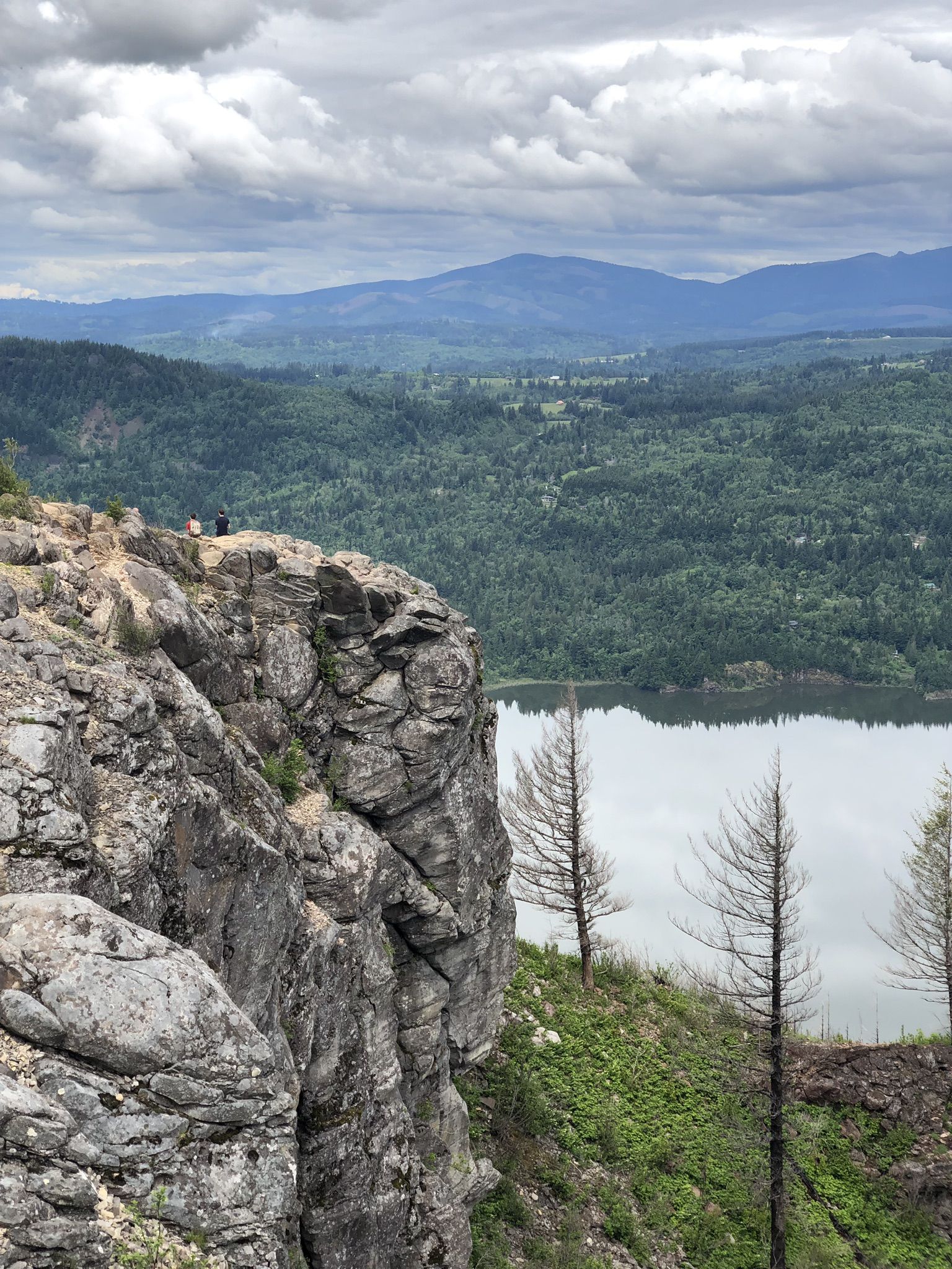 Two people on a rocky cliff overlooking a wide river and distant mountains. - Angel's Rest and Devil's Rest — Columbia River Gorge