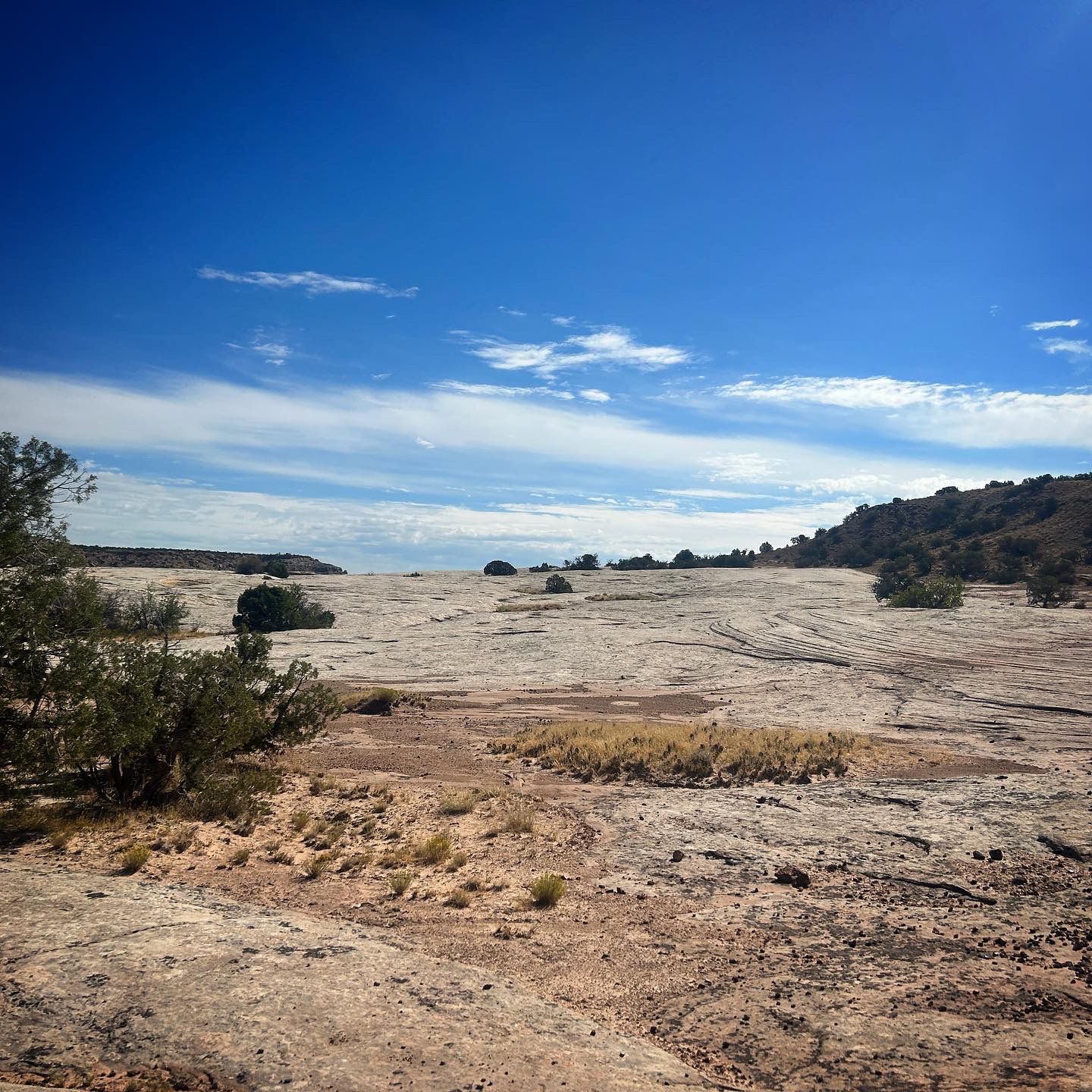 Expansive rocky desert landscape under a bright blue sky with scattered clouds. - Top of the World Trail