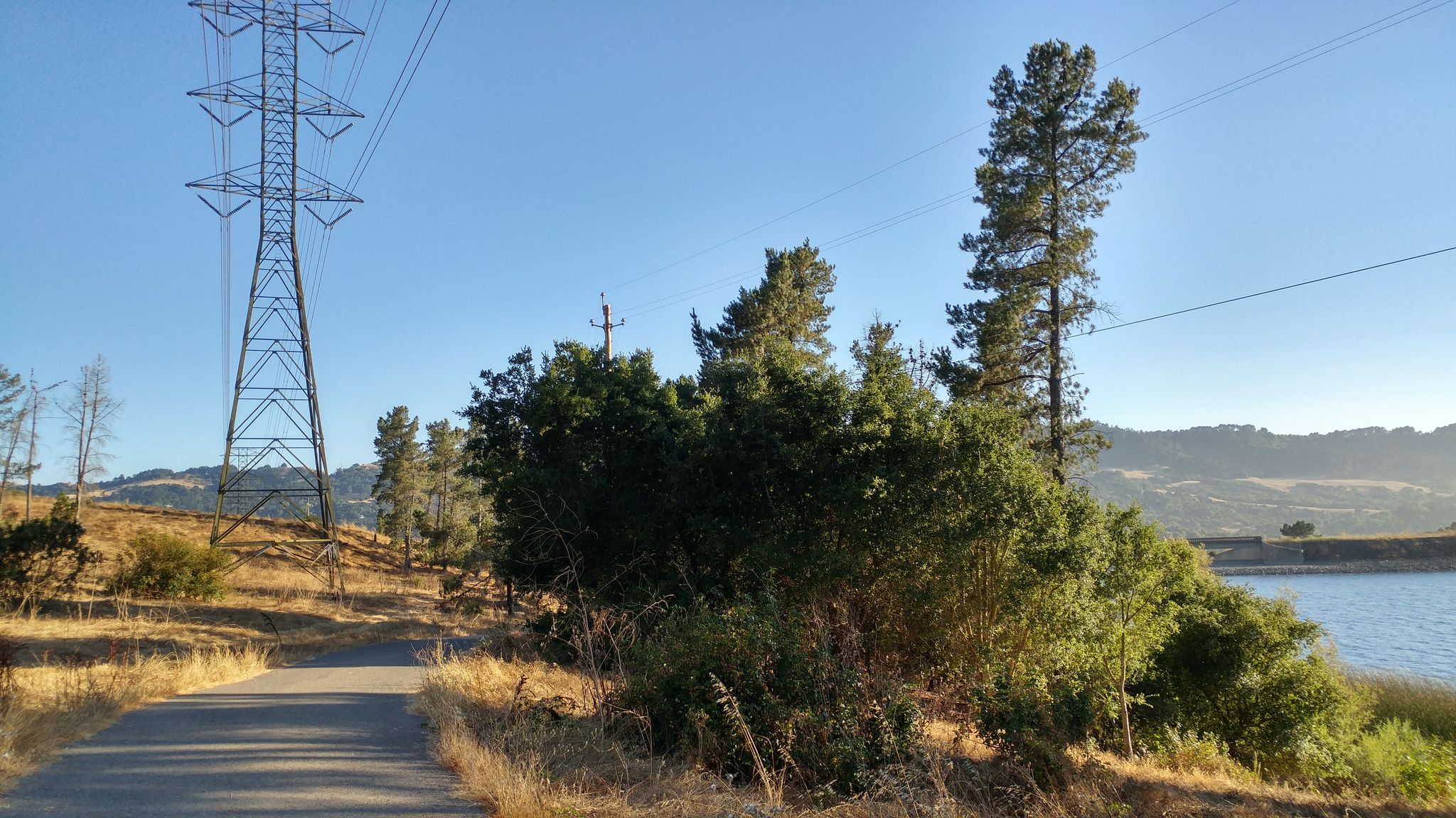 A paved path next to a lake, with a power line tower and trees. - Oursan and Bear Creek Trail Loop