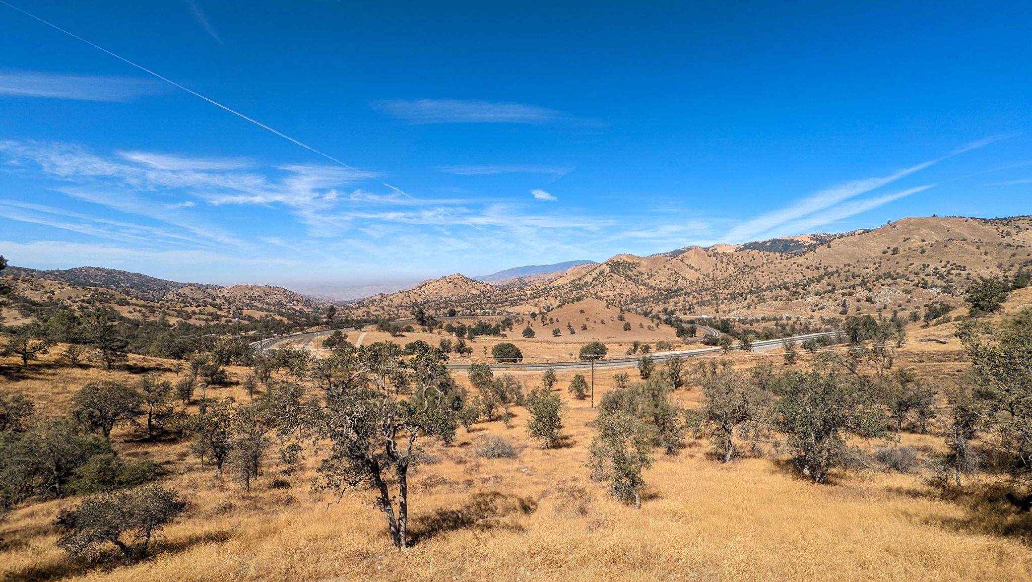 Sunny valley with dry hills, scattered trees, and a winding road. - Bakersfield to Tehachapi loop