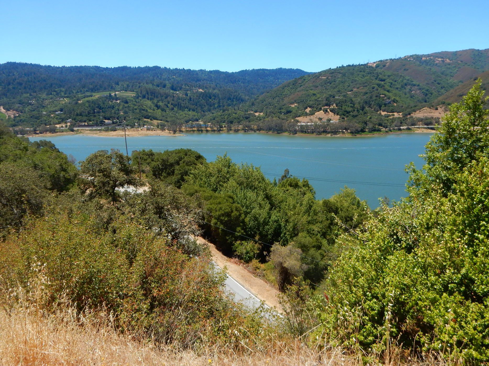 A serene lake surrounded by lush green hills under a clear blue sky. - Bay Area Ridge Trail: Priest Rock to Kennedy Knob