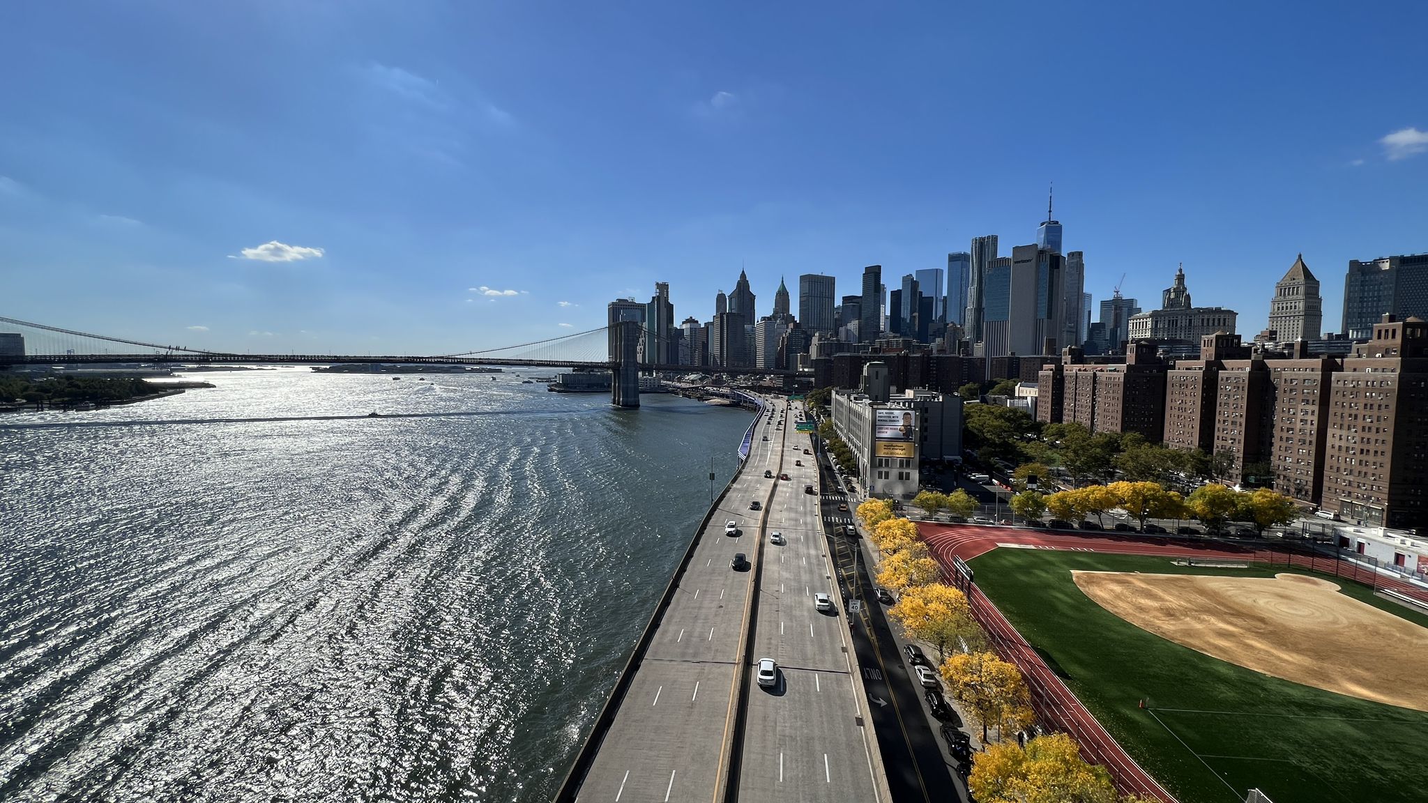 Elevated view of a highway, river, city skyline, and sports field. - Titanic Memorial Lighthouse – Pier 17 loop from Wall Street