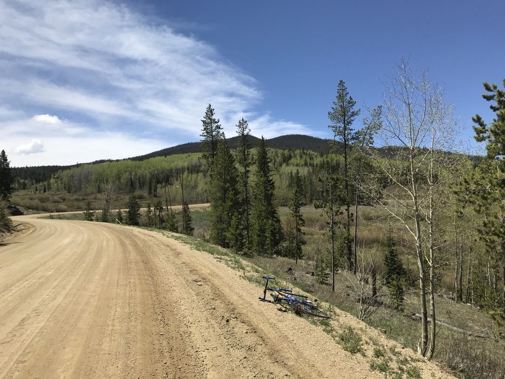 A dirt road winds through a sunny mountain landscape with a bicycle. - Fraser – Colorado River loop from Fraser-Winter Park