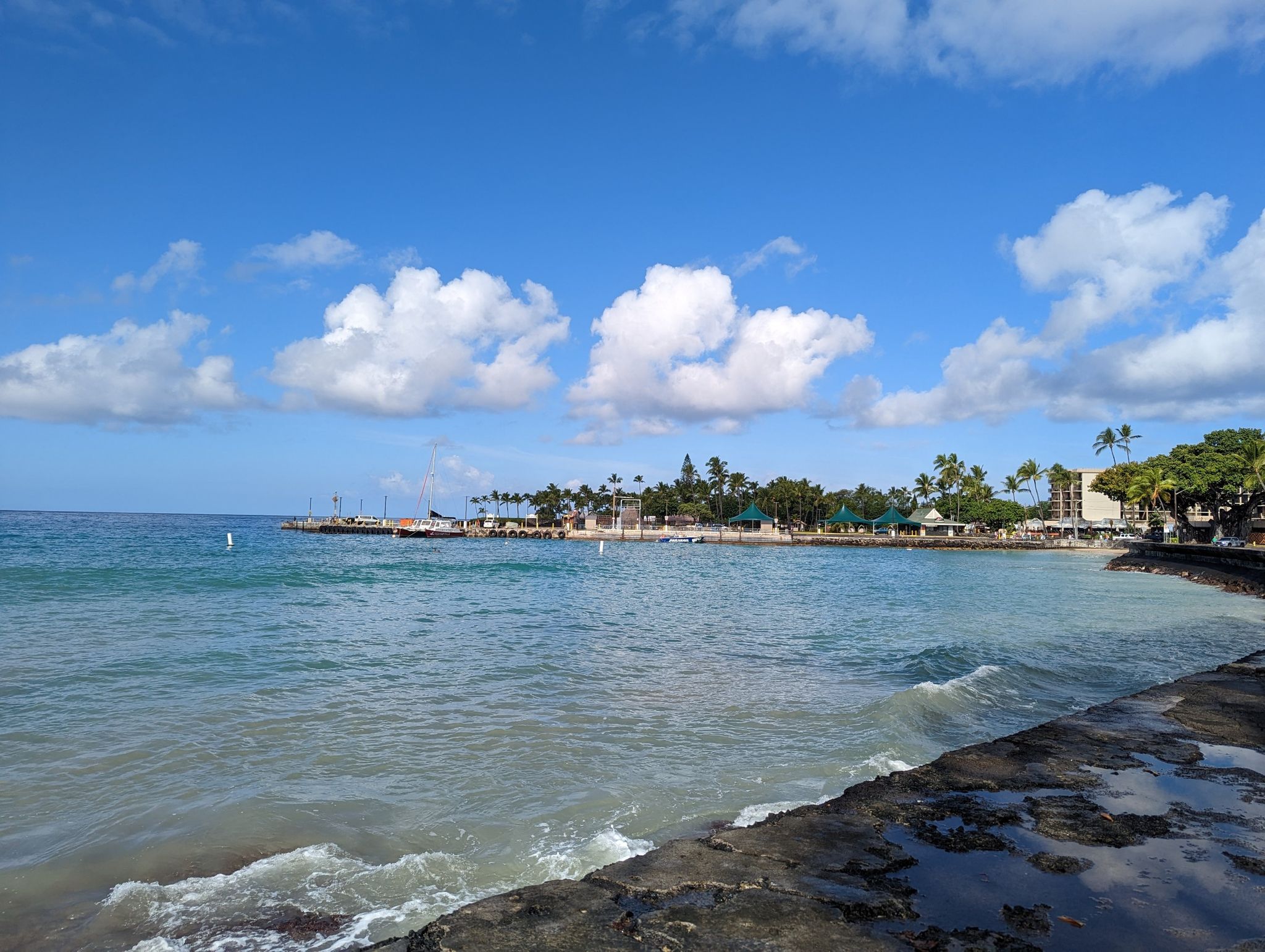 Bright ocean view with distant coastal buildings under a blue sky. - Keauhou to Lava Tube