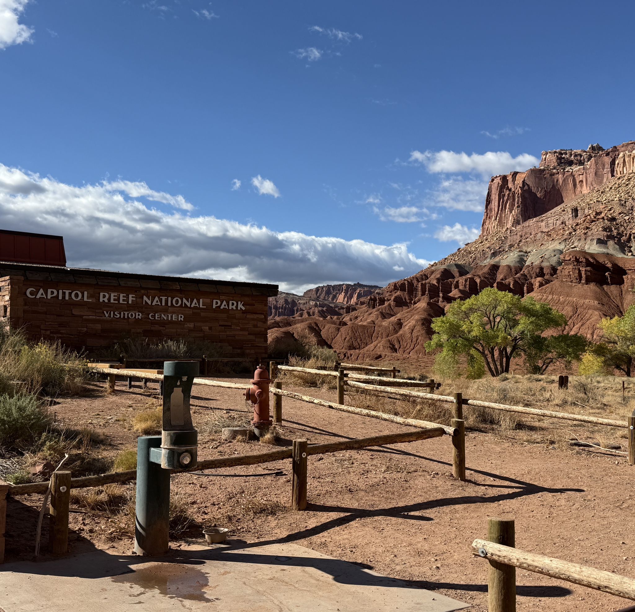 A wooden sign and split-rail fence line a dirt path near red rock formations. - Sulphur Creek Trail