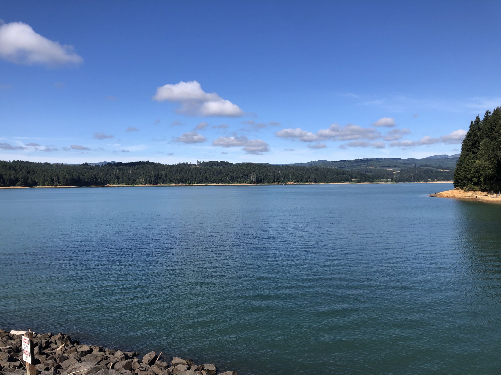 Vast blue lake under a bright sky, surrounded by green forested hills. - Roadbike loop from Forest Grove
