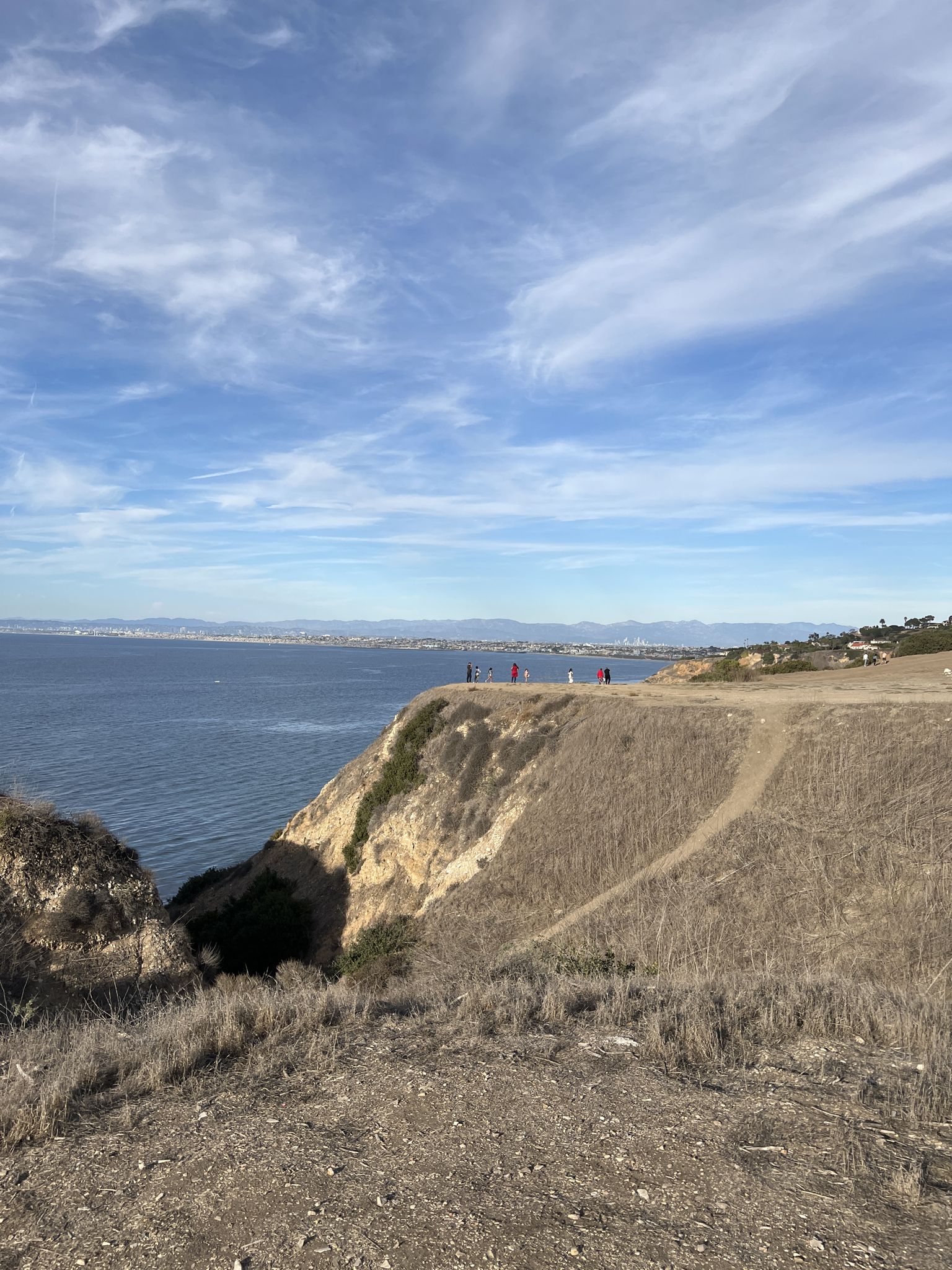 Sunny view of a steep cliff overlooking the ocean with distant people. - Malaga Lunada Vista Loop