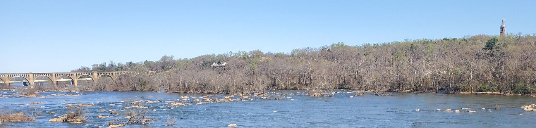 Panoramic view of a wide river with rapids, a distant bridge, and bare trees. - Pump House Park – Maymont Park loop from Bon Air