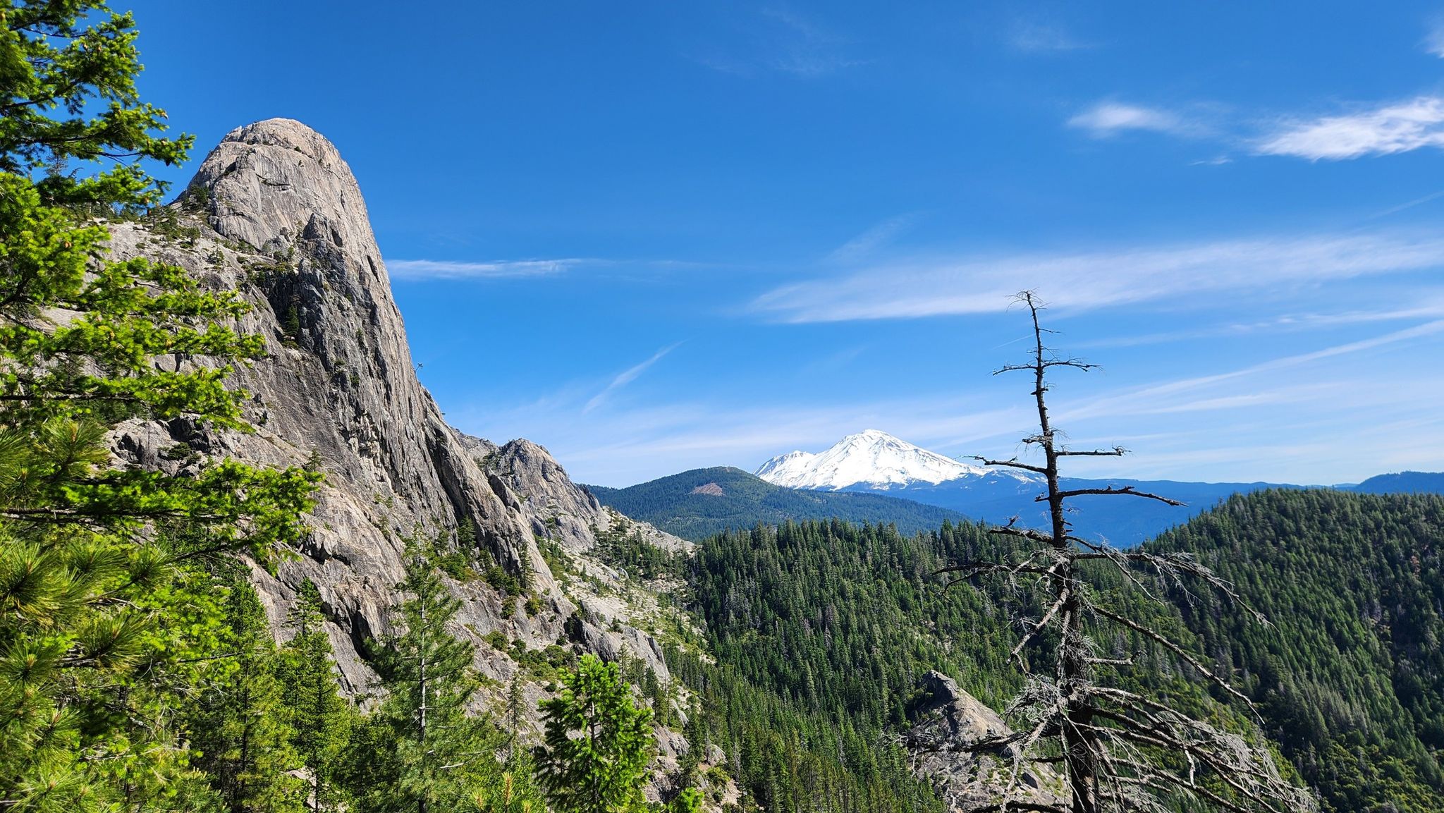 Sunny view of a large rock formation, forested mountains, and a distant snow-capped peak. - Crags Trail to Castle Dome