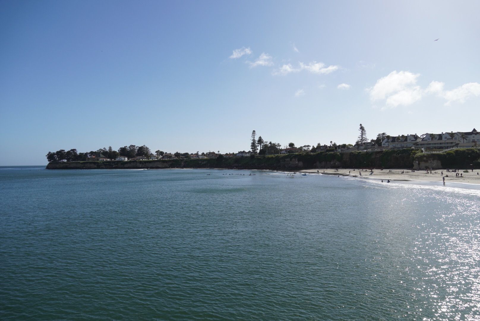 Sunny ocean view with distant beach, cliffs, and buildings under blue sky. - Santa Cruz Beach Boardwalk – Downtown Santa Cruz Mural loop from Santa Cruz