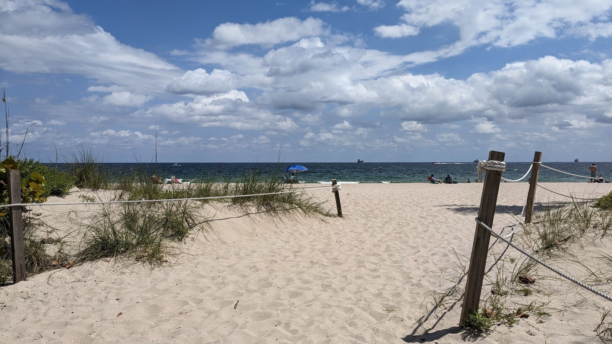 Sandy beach path leading to the ocean under a bright, partly cloudy sky. - Barrier Islands Greenway