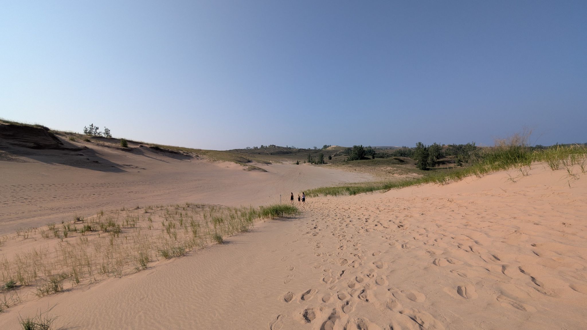Wide sandy path through dunes with distant people under a clear blue sky. - Sleeping Bear Point Trail