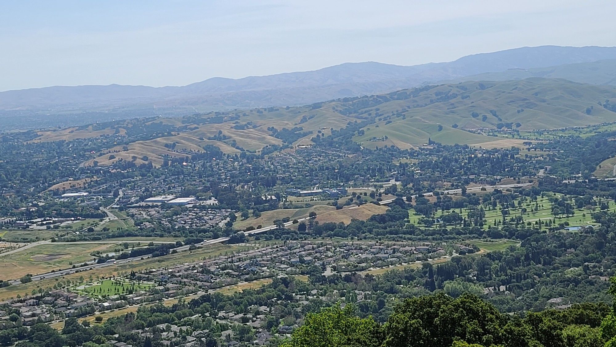 A panoramic view of a valley with urban areas nestled among rolling hills. - Augustin Bernal Community Park – Pleasanton Ridge viewpoint loop from Pleasanton Ridge Regional Park