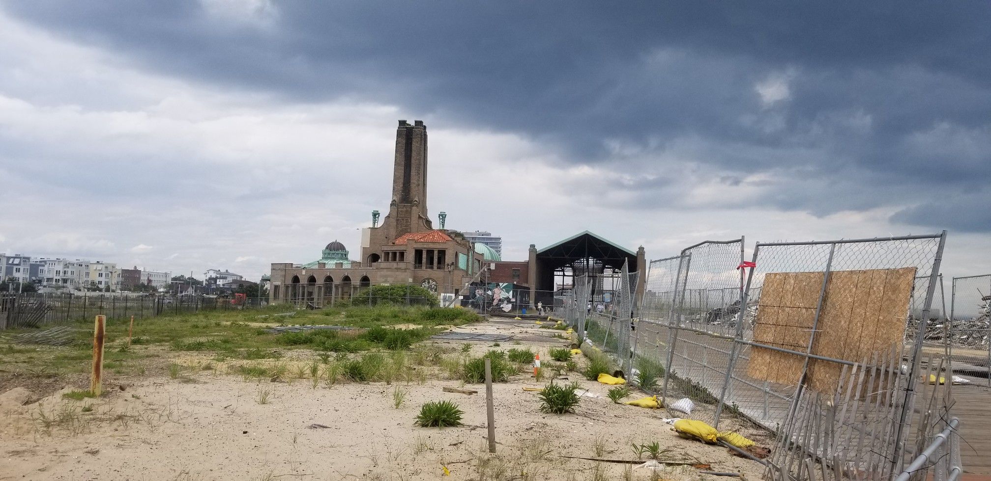 Large old building with a tower, construction fence, and a cloudy sky. - Hiking loop from Neptune City