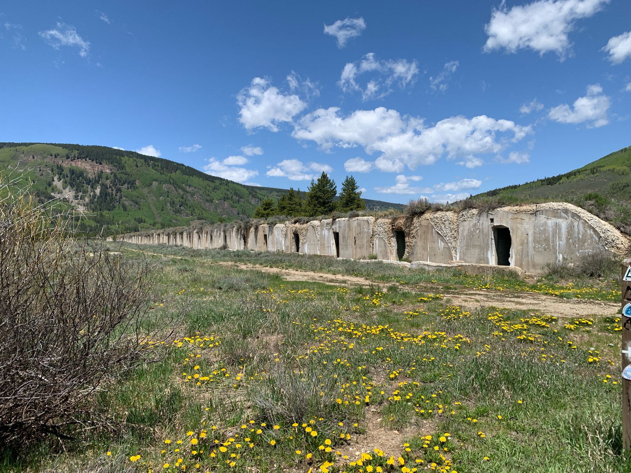 A long concrete structure with arched openings stretches across a sunny field. - Colorado Trail: Camp Hale Loop
