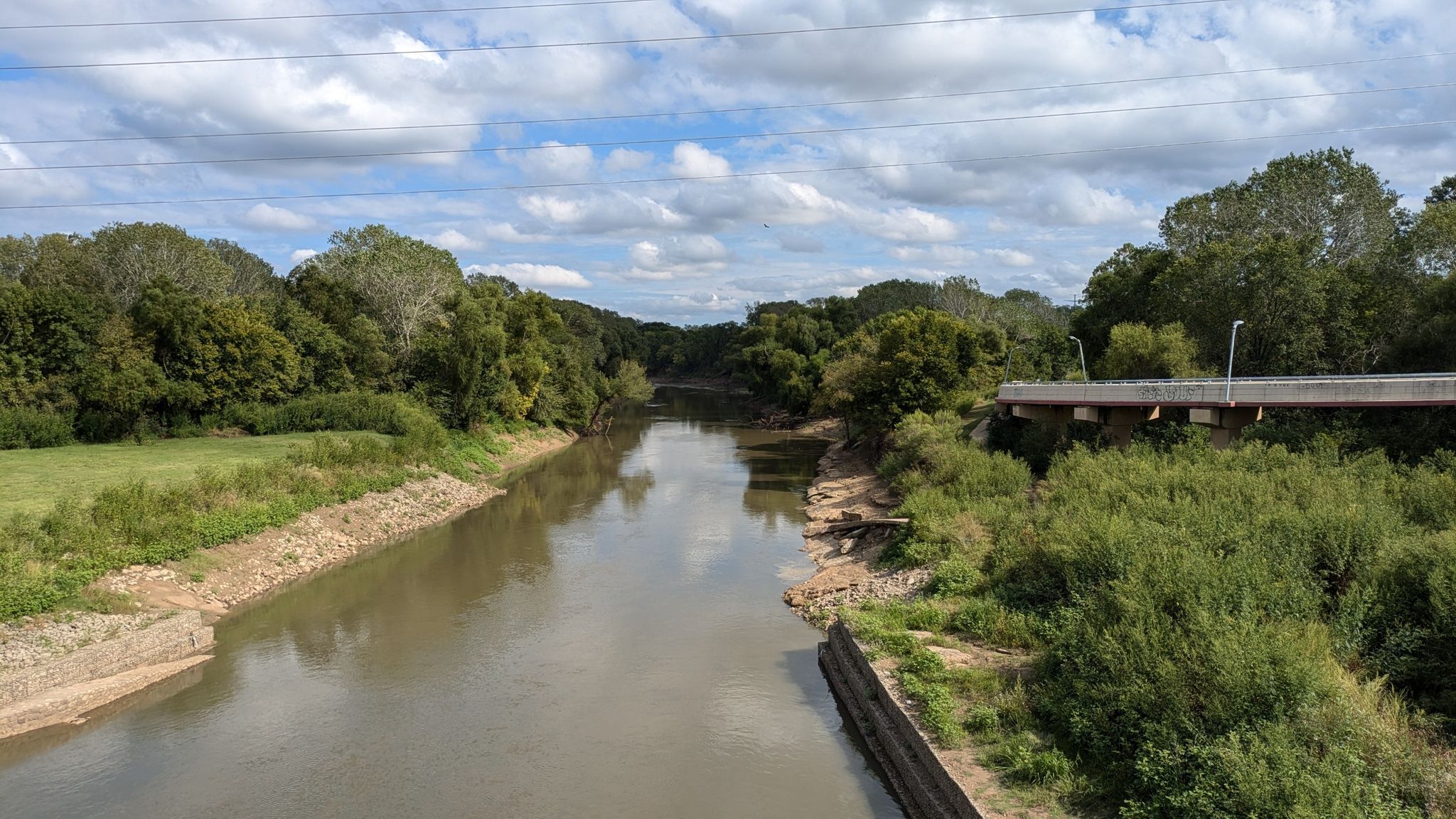 A wide river flowing between green banks under a cloudy sky. - Trinity Skyline Trail