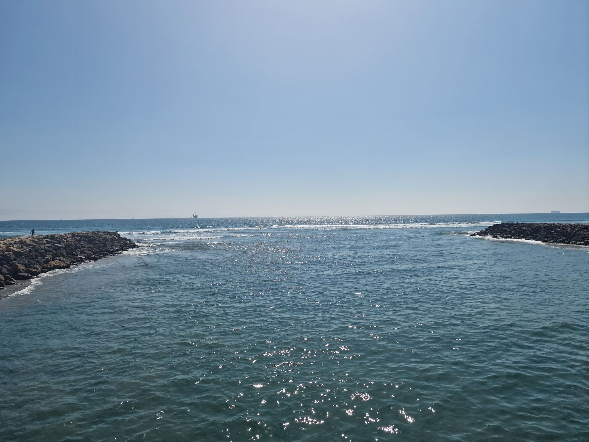 Ocean inlet with rock jetties under a bright, clear blue sky. - Bolsa Chica Ecological Reserve Trail
