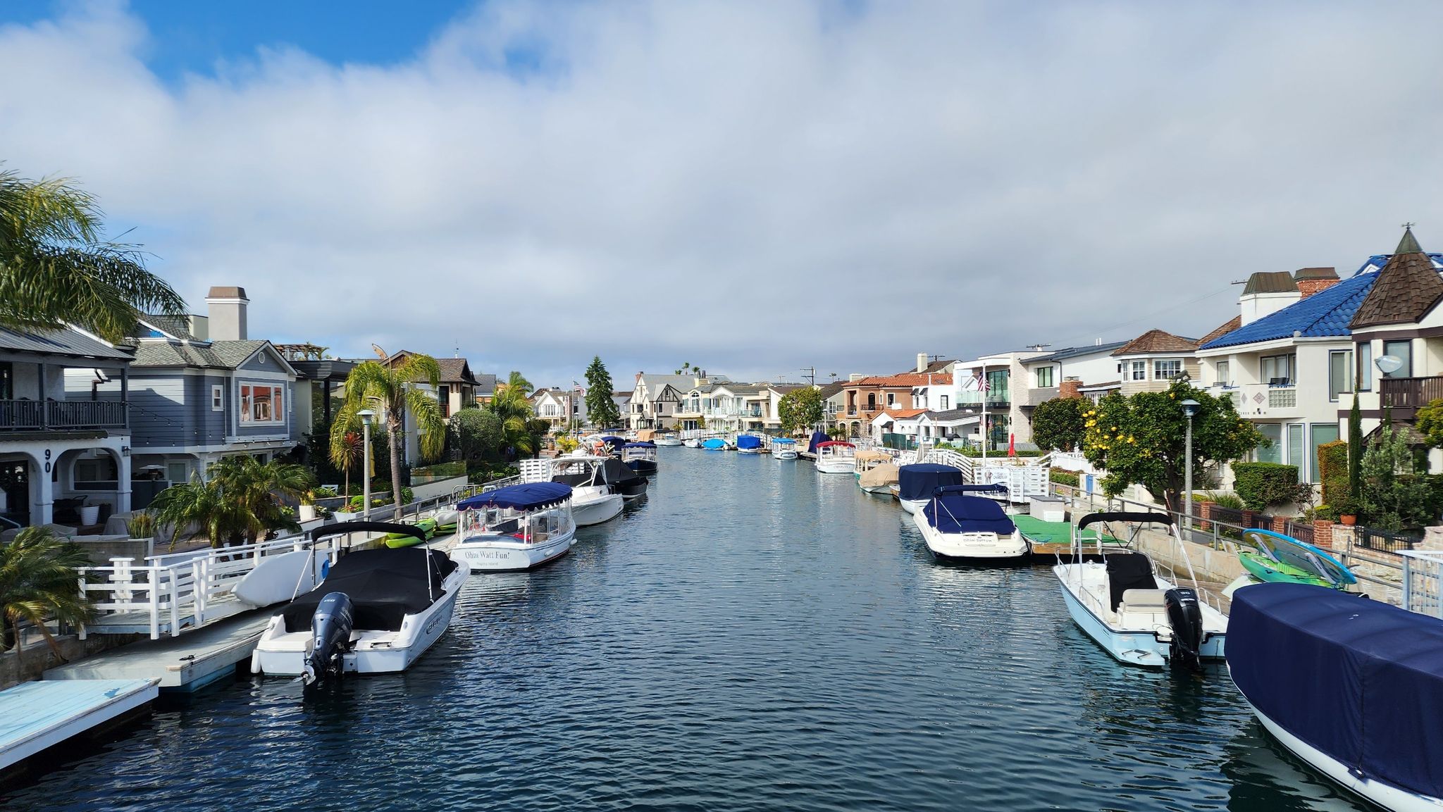 Boats docked along a canal lined with houses under a partly cloudy sky. - Naples Island Canals loop from Naples Islands