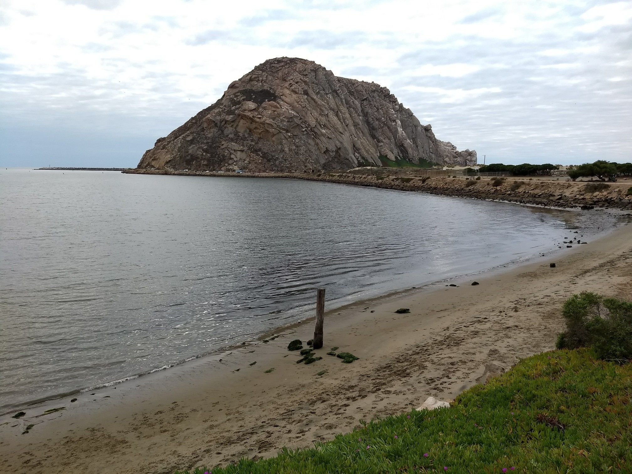 Large rocky mountain overlooking a calm bay and sandy beach. - Morro Bay — National Estuary – Anchor Memorial Park loop from Morro Bay
