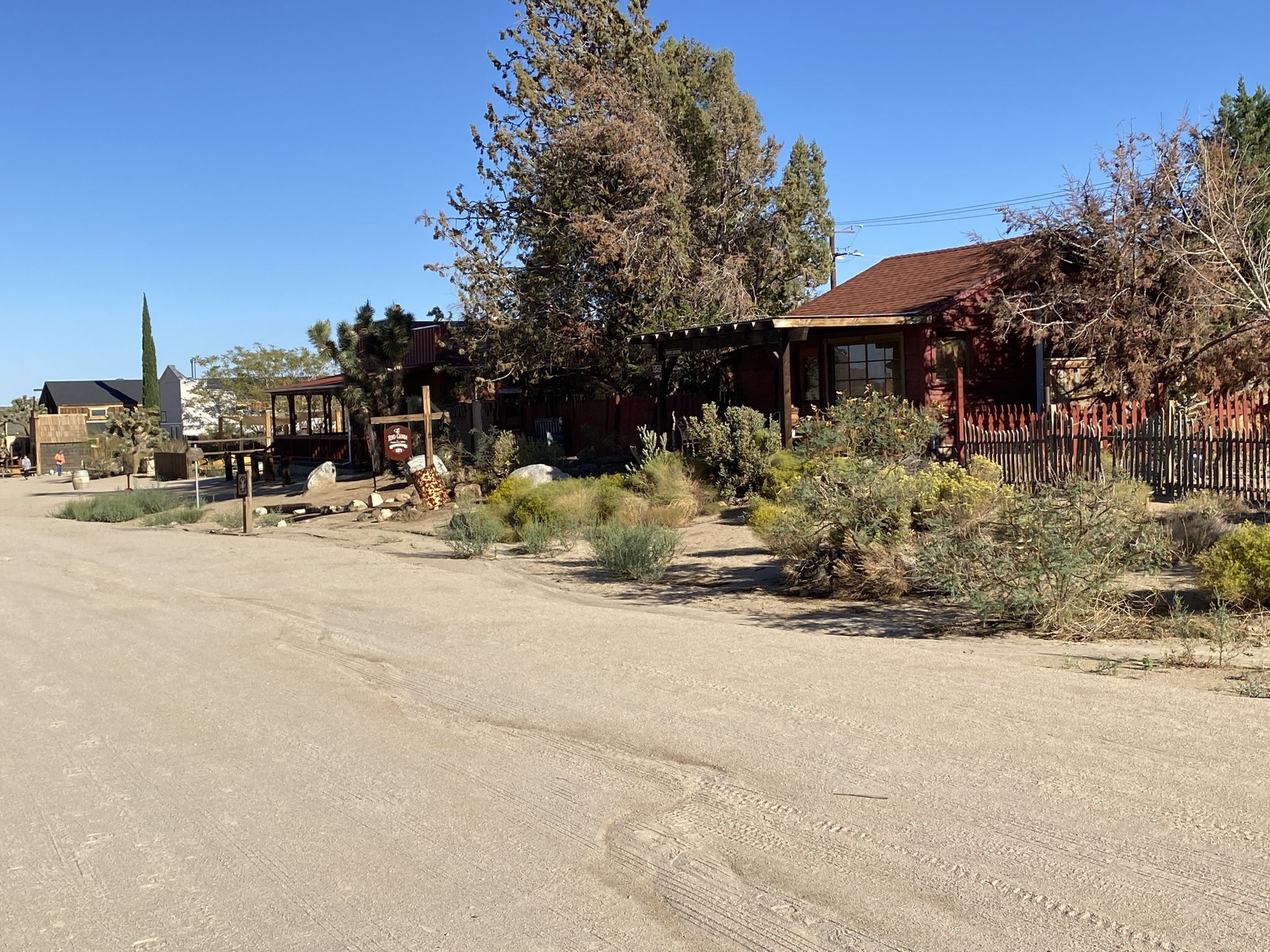 Rustic buildings and trees line a dirt road on a bright day. - Pioneertown loop from Pioneertown