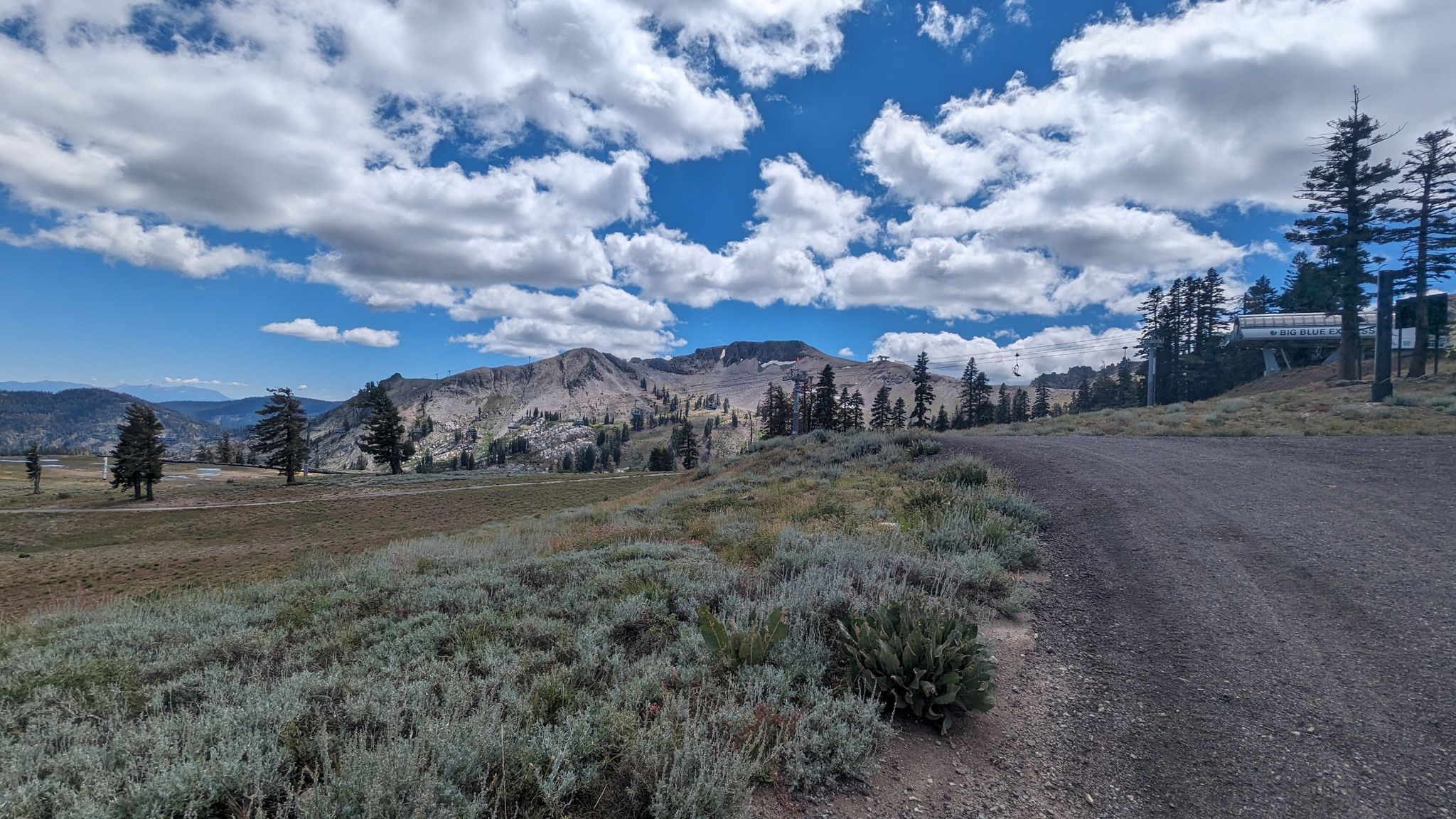 Dirt road winding through a mountain landscape with green vegetation under a cloudy sky. - Western States Trail Loop