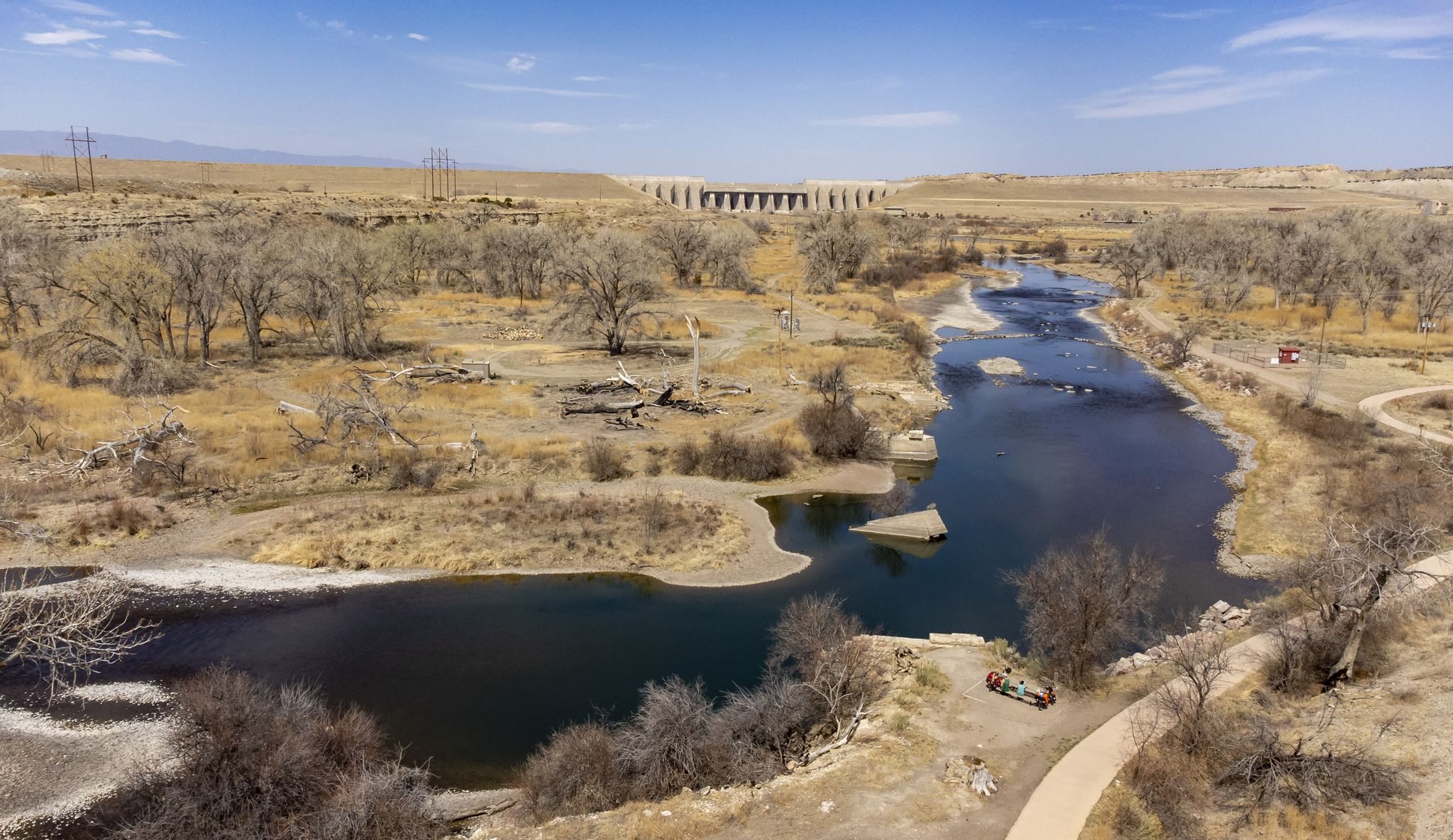 Aerial view of a river, dry landscape, and a distant dam on a sunny day. - Arkansas River and Pueblo Reservoir Trail Loop