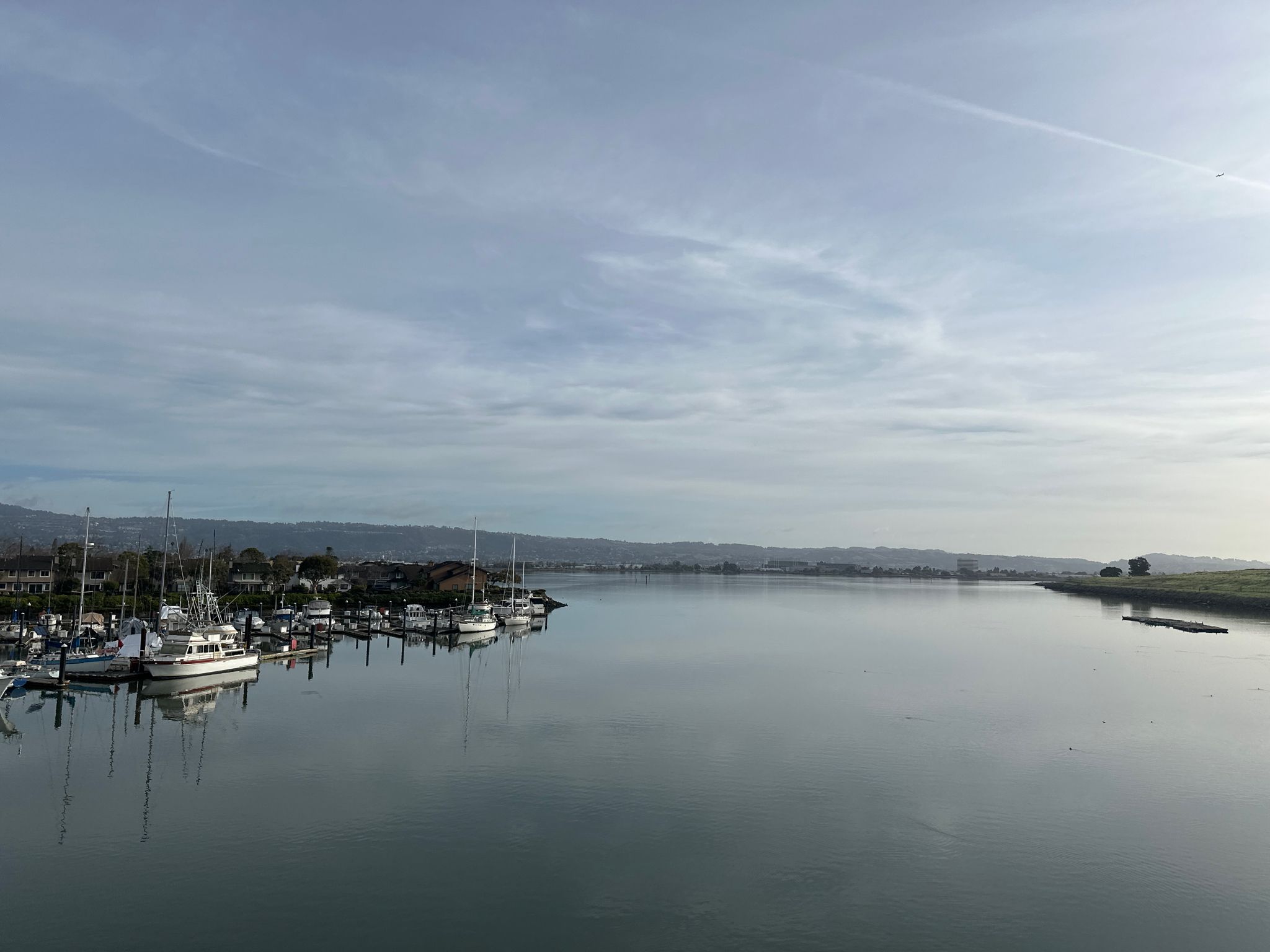 A marina with boats docked on calm water, distant hills, and cloudy sky. - Overlooks of San Francisco Bay loop from Alameda