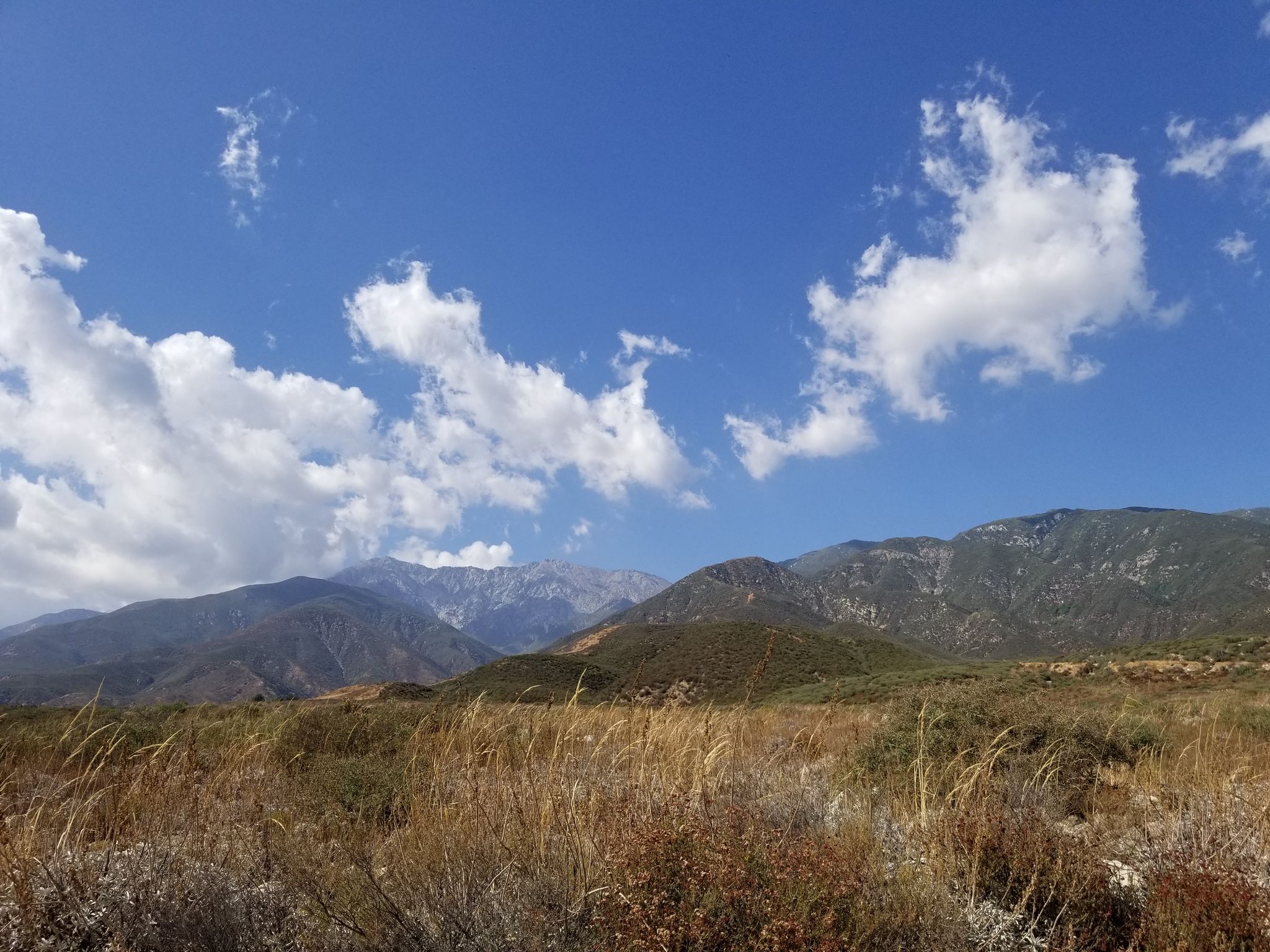 Expansive view of dry grassy hills and distant mountains under a blue sky. - Etiwanda Falls Trail