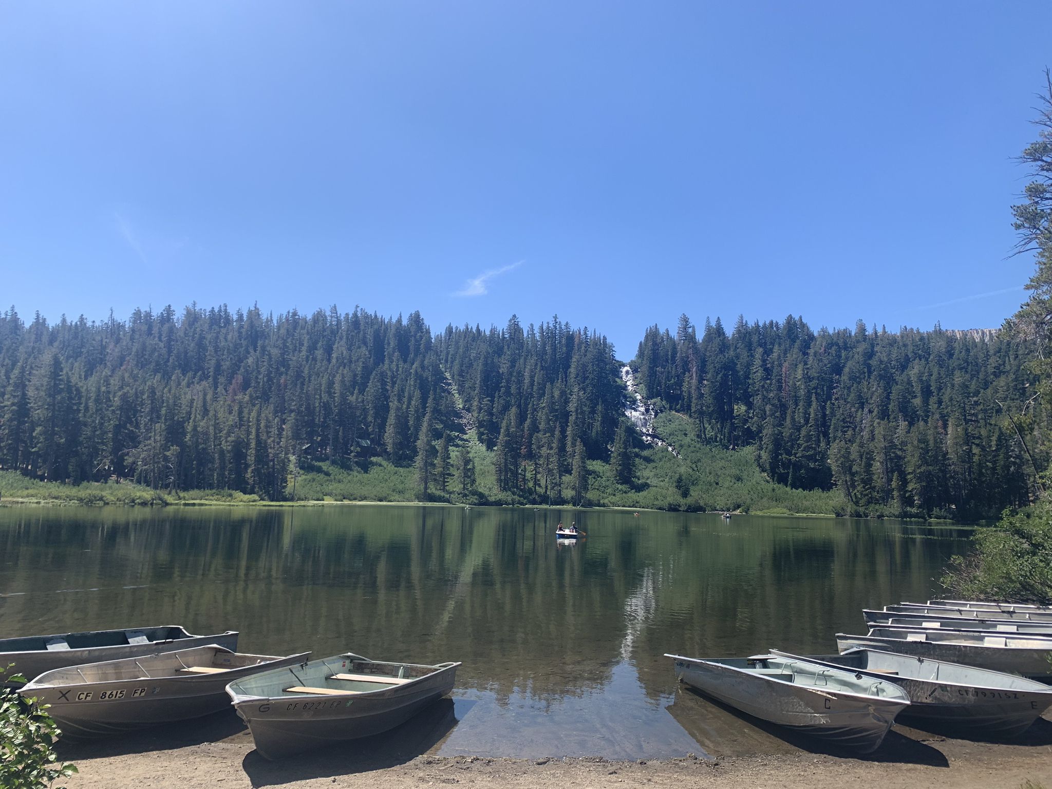 Empty rowboats on a lake shore, with a forested hillside and waterfall. - Twin Lakes – Twin Lakes loop from Twin Lakes