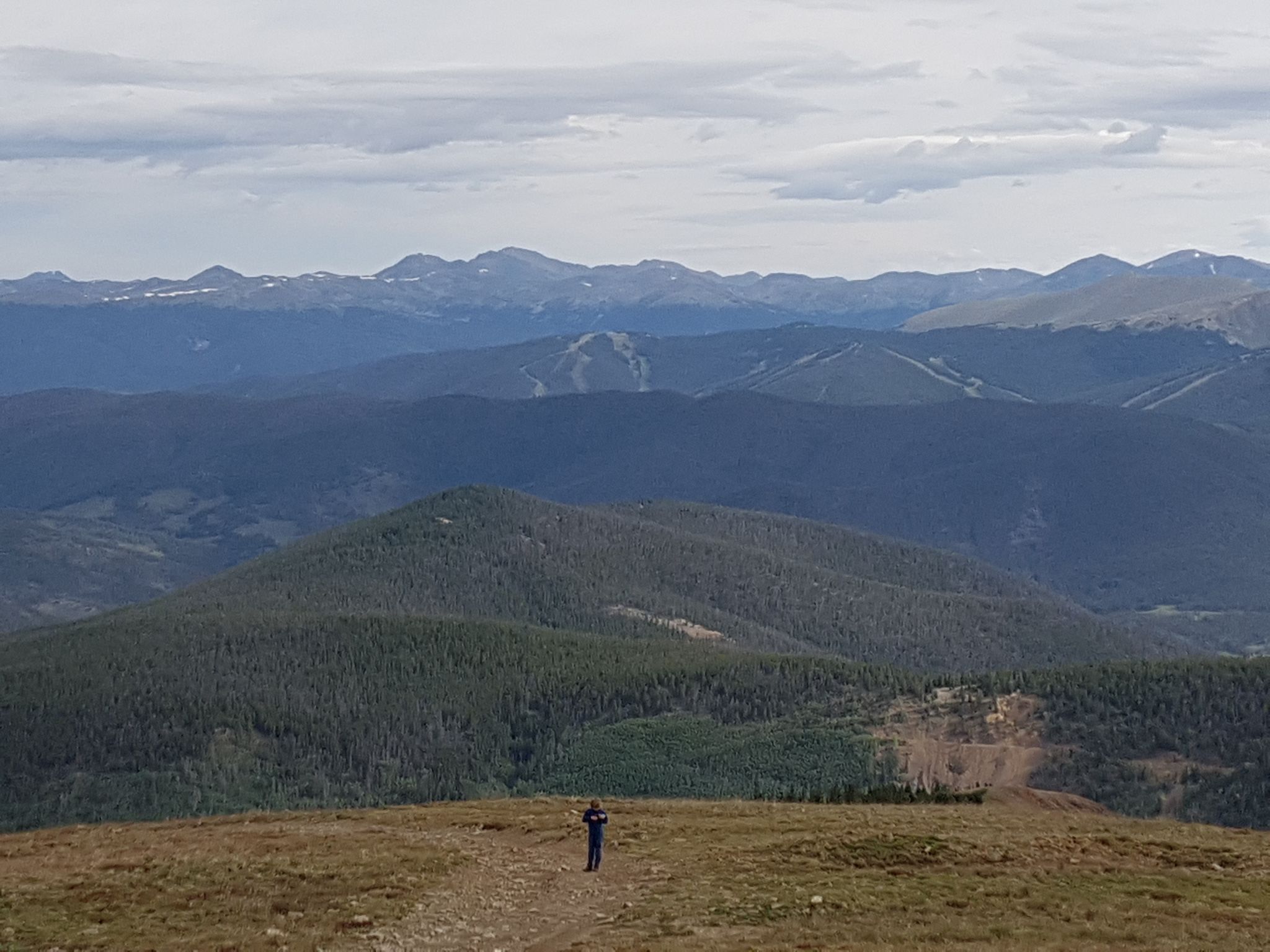 A person stands on a ridge overlooking a vast mountain range. - Bald Mountain via Baldy Road