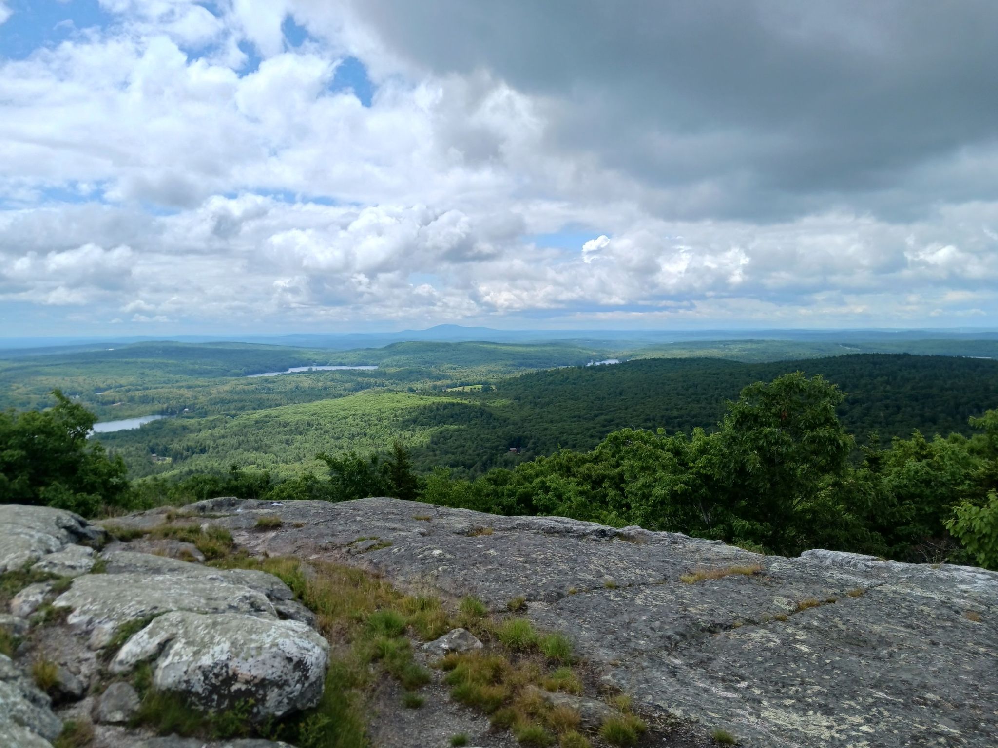 Vast green forest and distant lakes seen from a rocky mountain top under cloudy skies. - Watatic Summit