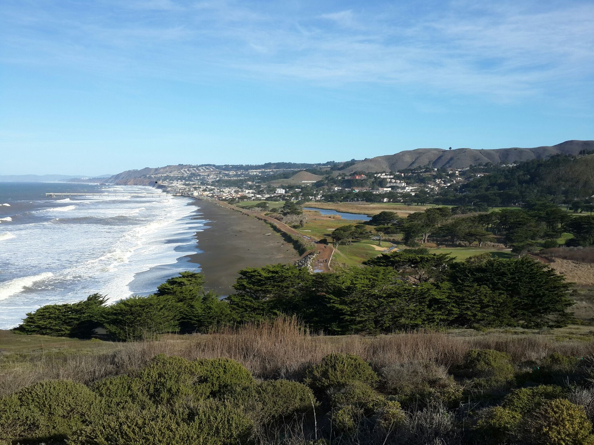 Panoramic coastal view with beach, town, and green hills under blue sky. - Pacifica Pier & Mori Point via Sharp Park Beach Promenade
