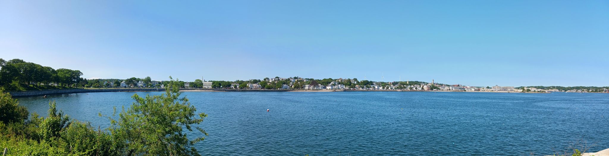 Panoramic view of a calm bay with a distant town under clear blue sky. - Stage Fort Trail