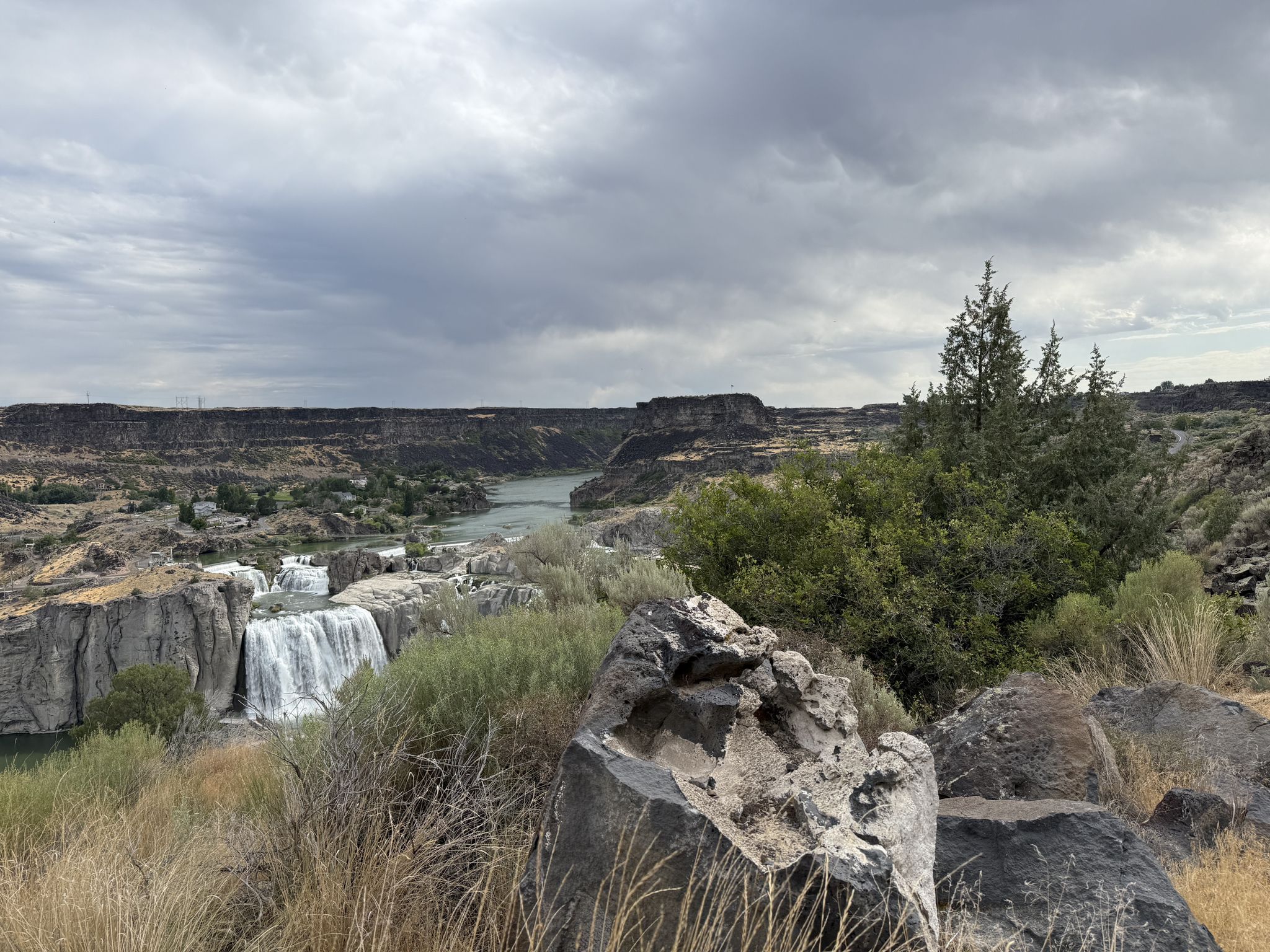 Waterfalls and a river in a canyon, with rocks and trees in foreground. - Shaded Stone Seating Area loop from Twin Falls Idaho Temple