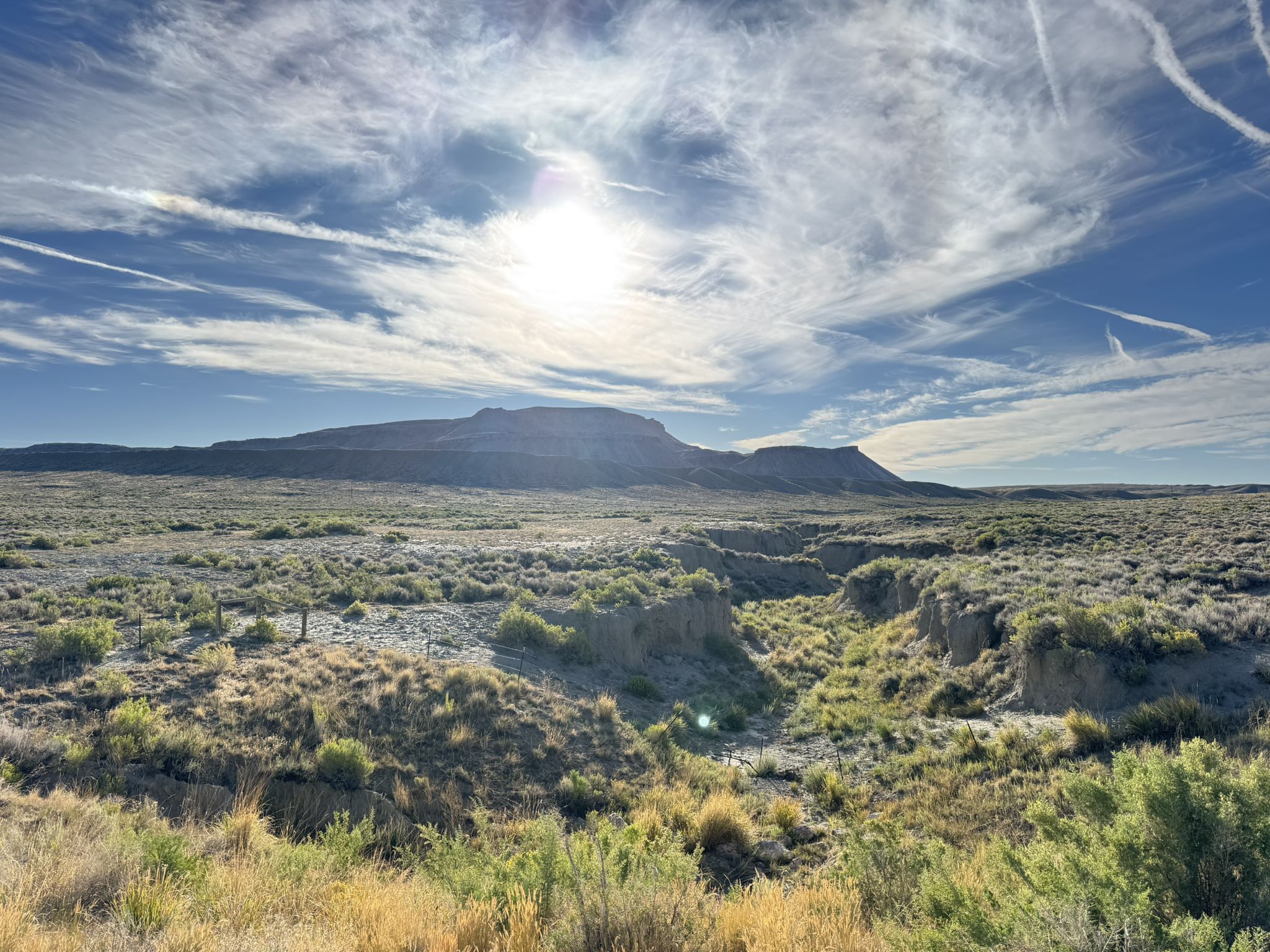 Bright sun over a vast desert landscape with a distant mesa and deep gully. - Sage Creek Road (Rawlins to Sage Creek)
