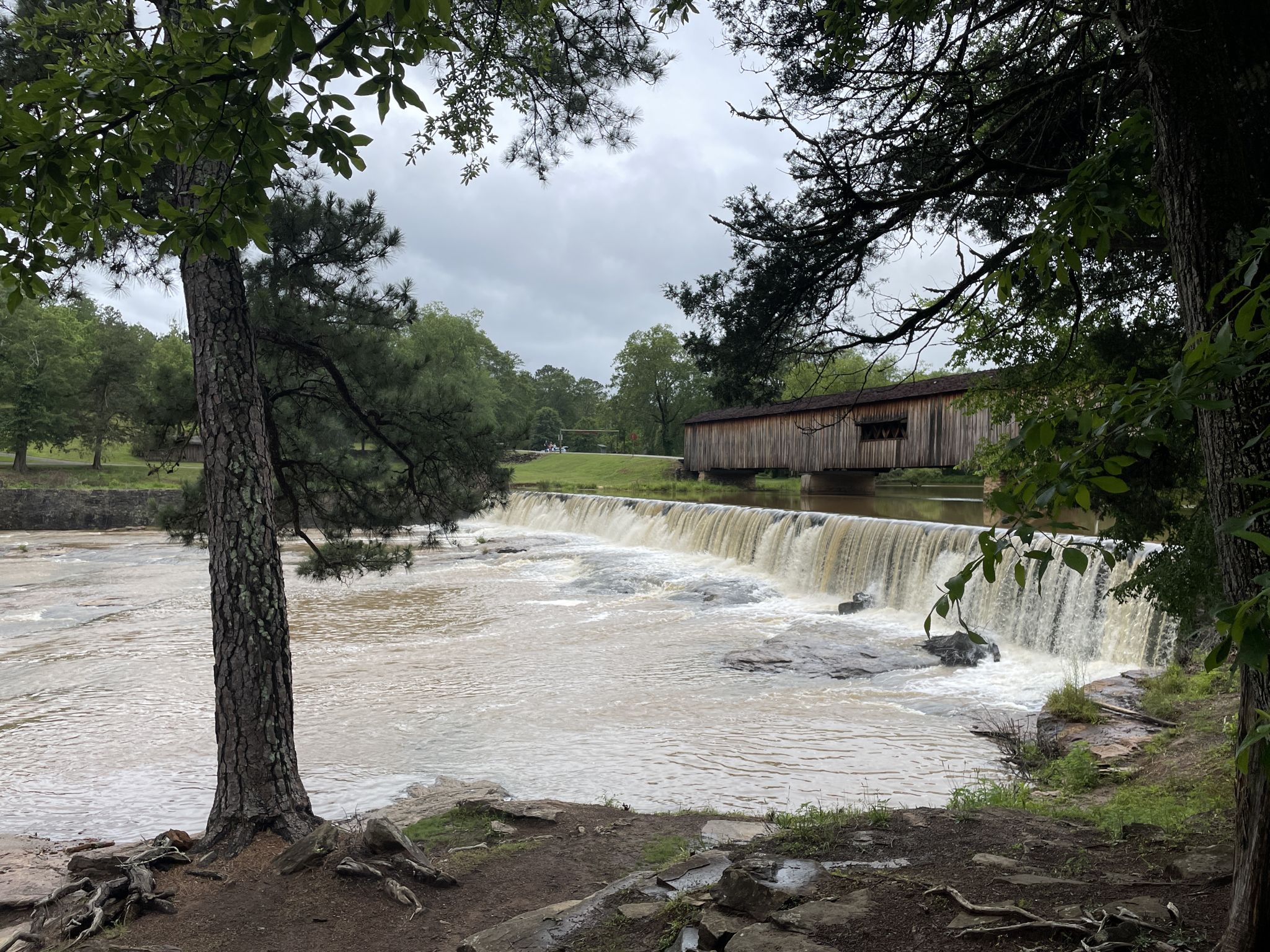 Overcast view of a waterfall and covered bridge, framed by trees. - Hiking and Biking Trail