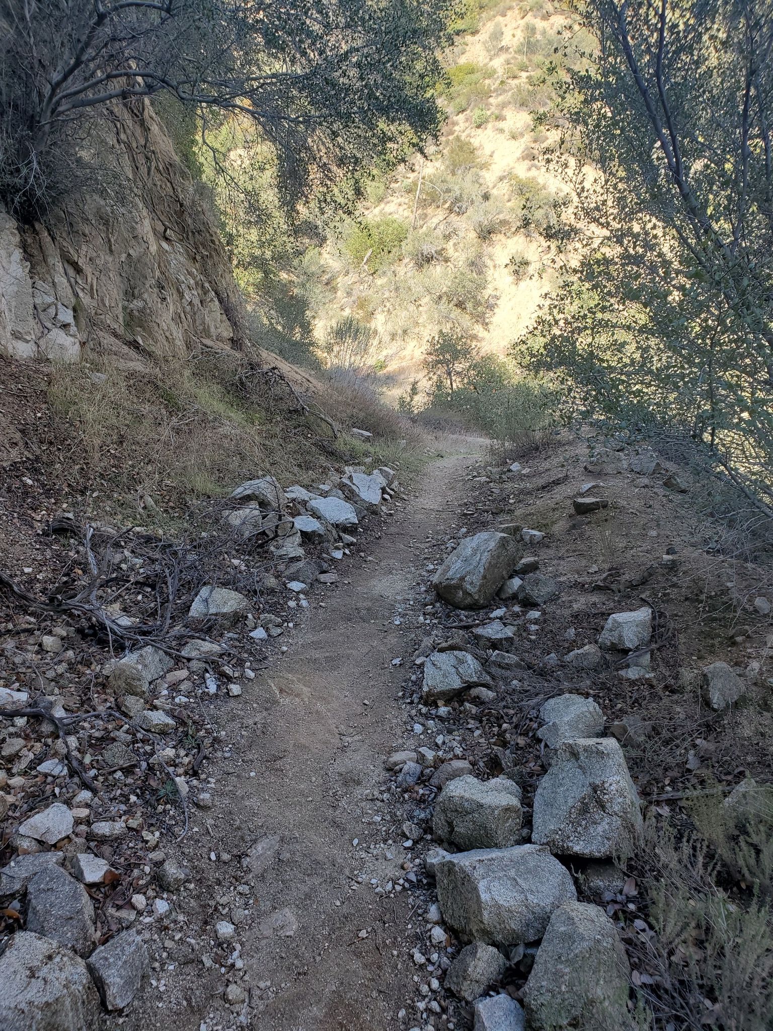 Narrow dirt trail winding through a rocky, sunlit mountain path. - Earl Canyon Motorway Trail