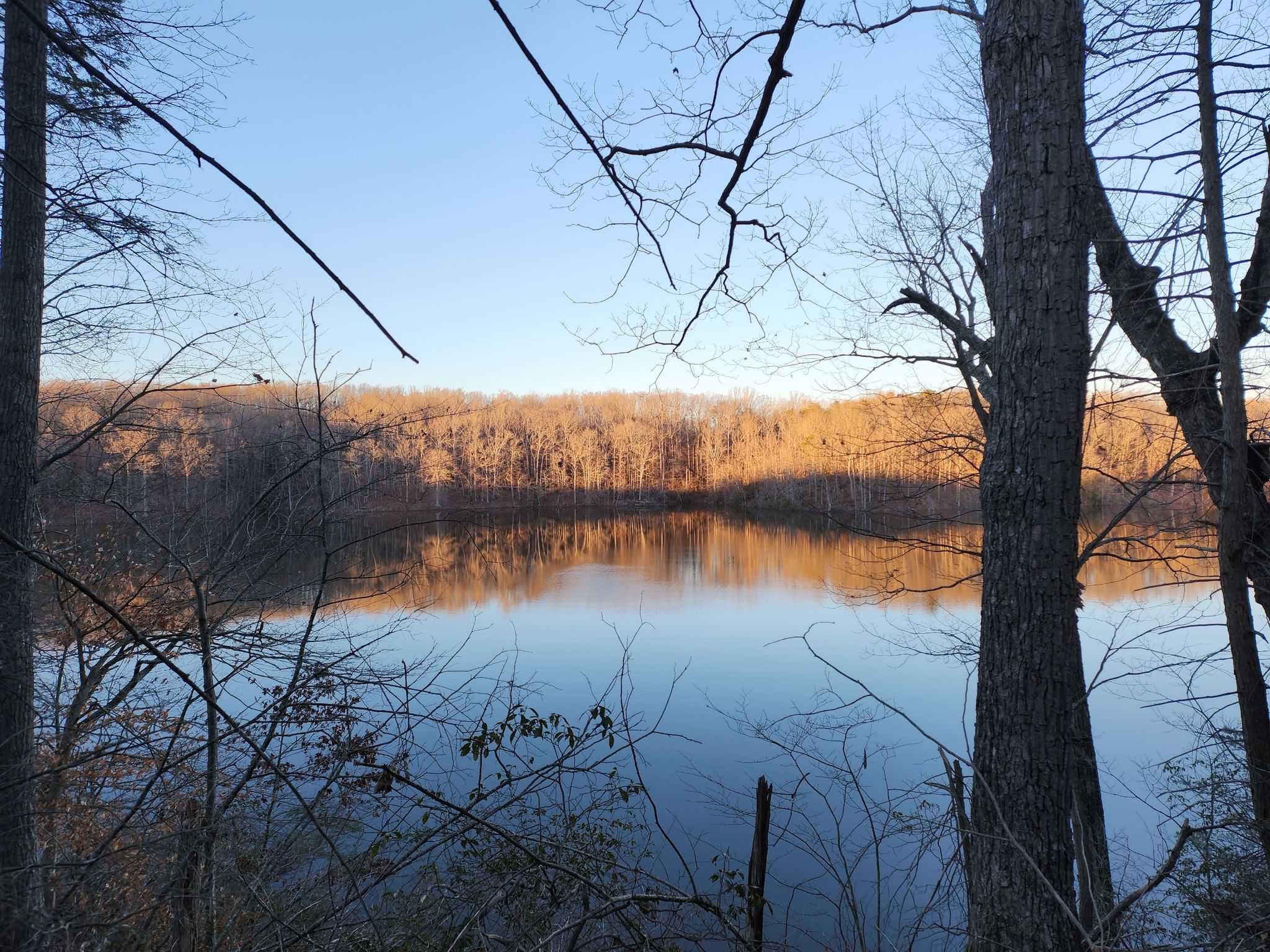A tranquil lake reflects bare trees under a golden evening sky. - Motts Run Hill – Motts Run loop from Motts Run Reservoir Recreation Area
