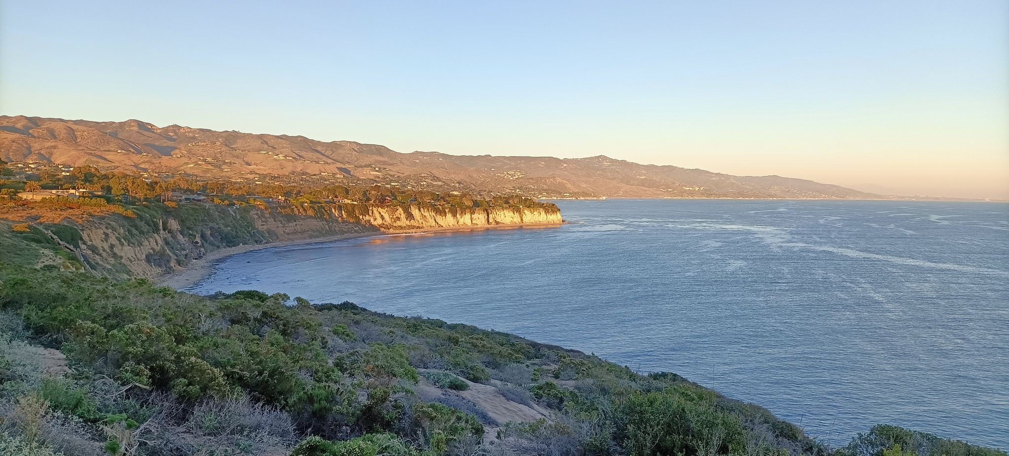 Coastal view with cliffs, ocean, and mountains under warm golden hour light. - Point Dume Cove Trail