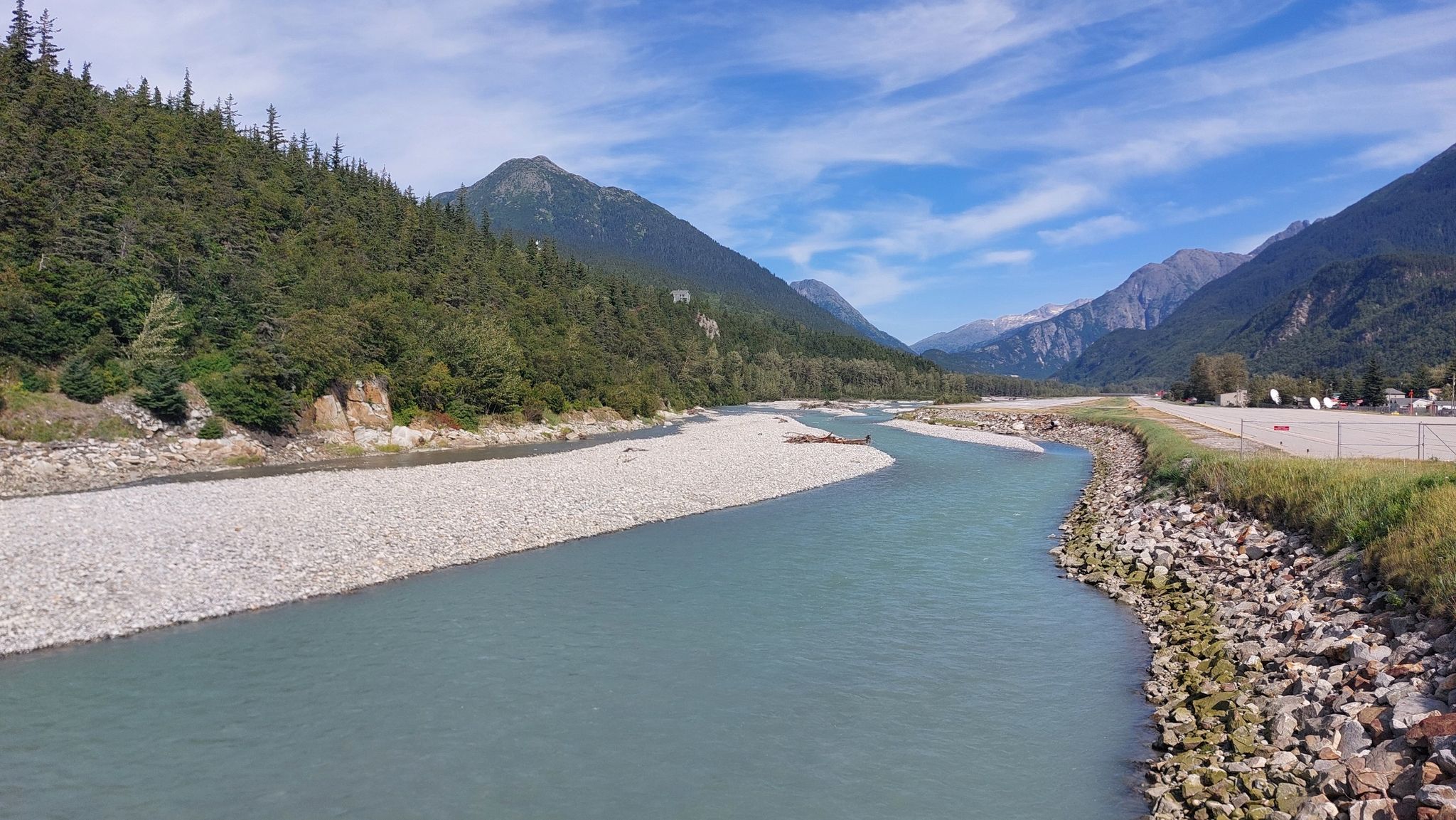 Wide river with gravel banks, forested mountains under a bright blue sky. - Yakutania Point and Smuggler's Cove Trail